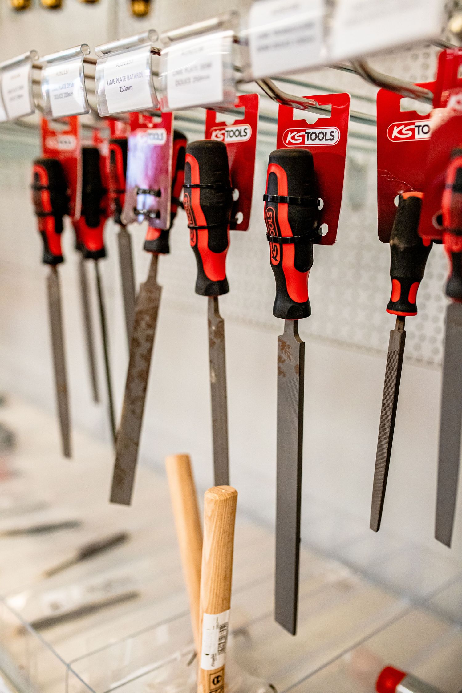 Row of red-handled KS Tools files and rasps hanging on display hooks.