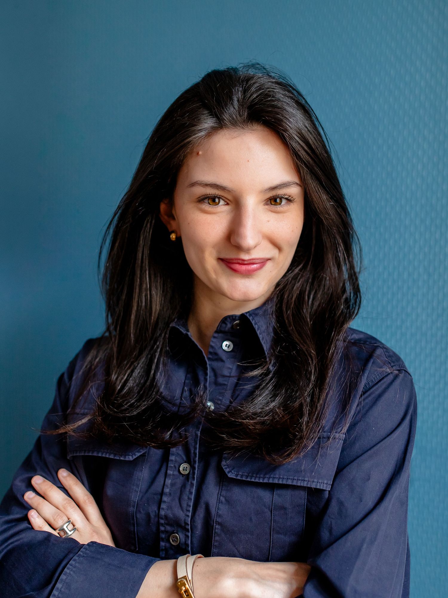 Professional portrait of a woman in a navy button-up shirt smiling against a blue background.