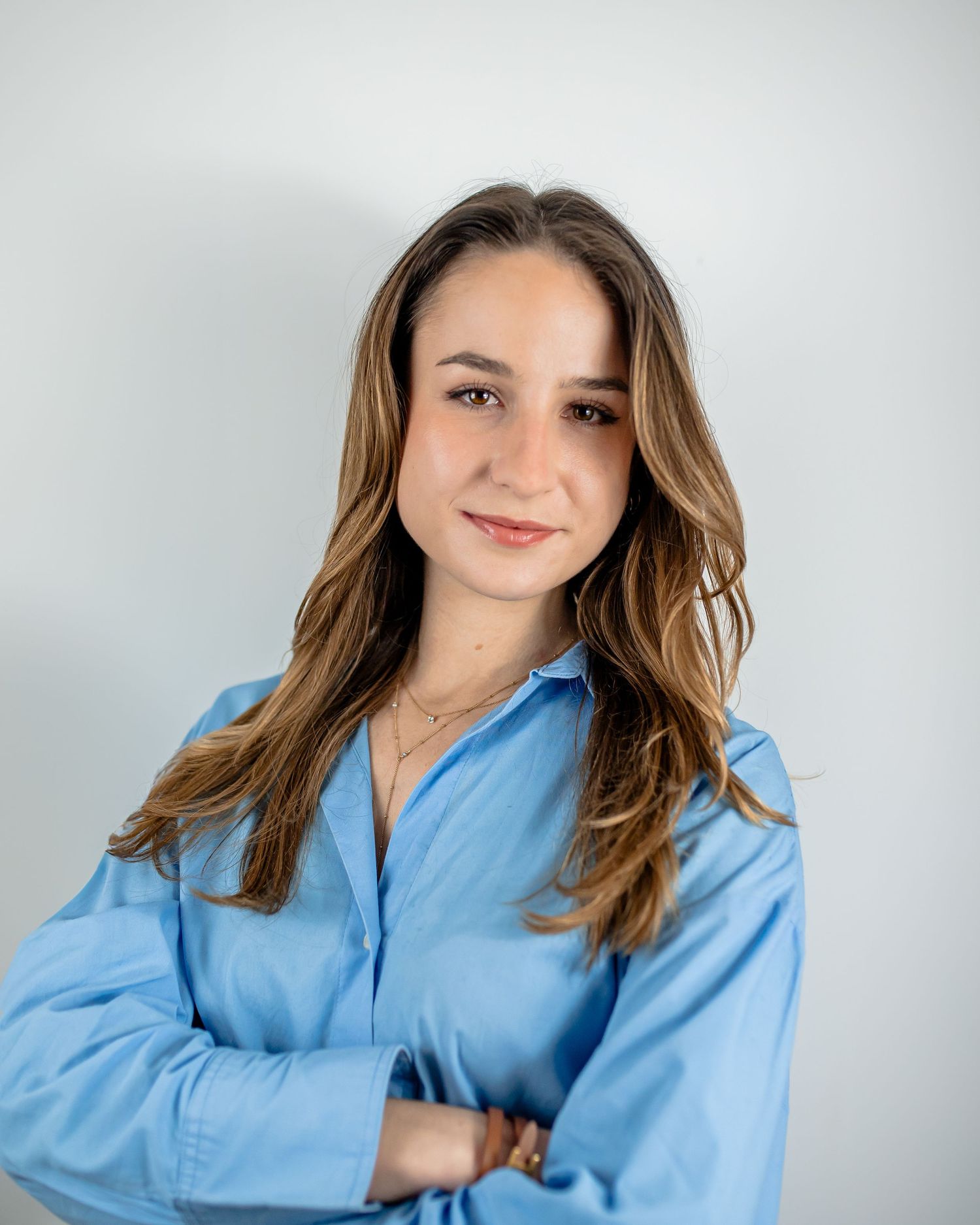 Professional headshot of someone in a blue shirt with long wavy hair against a white backdrop.