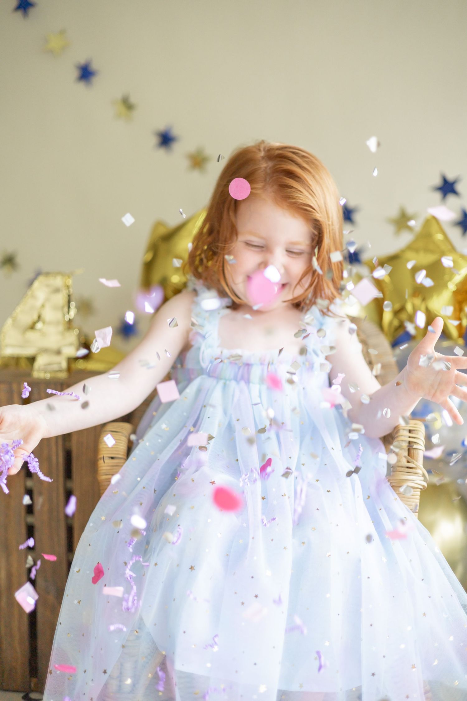 A child in a sparkly white party dress twirls among confetti and gold star decorations during a celebration.