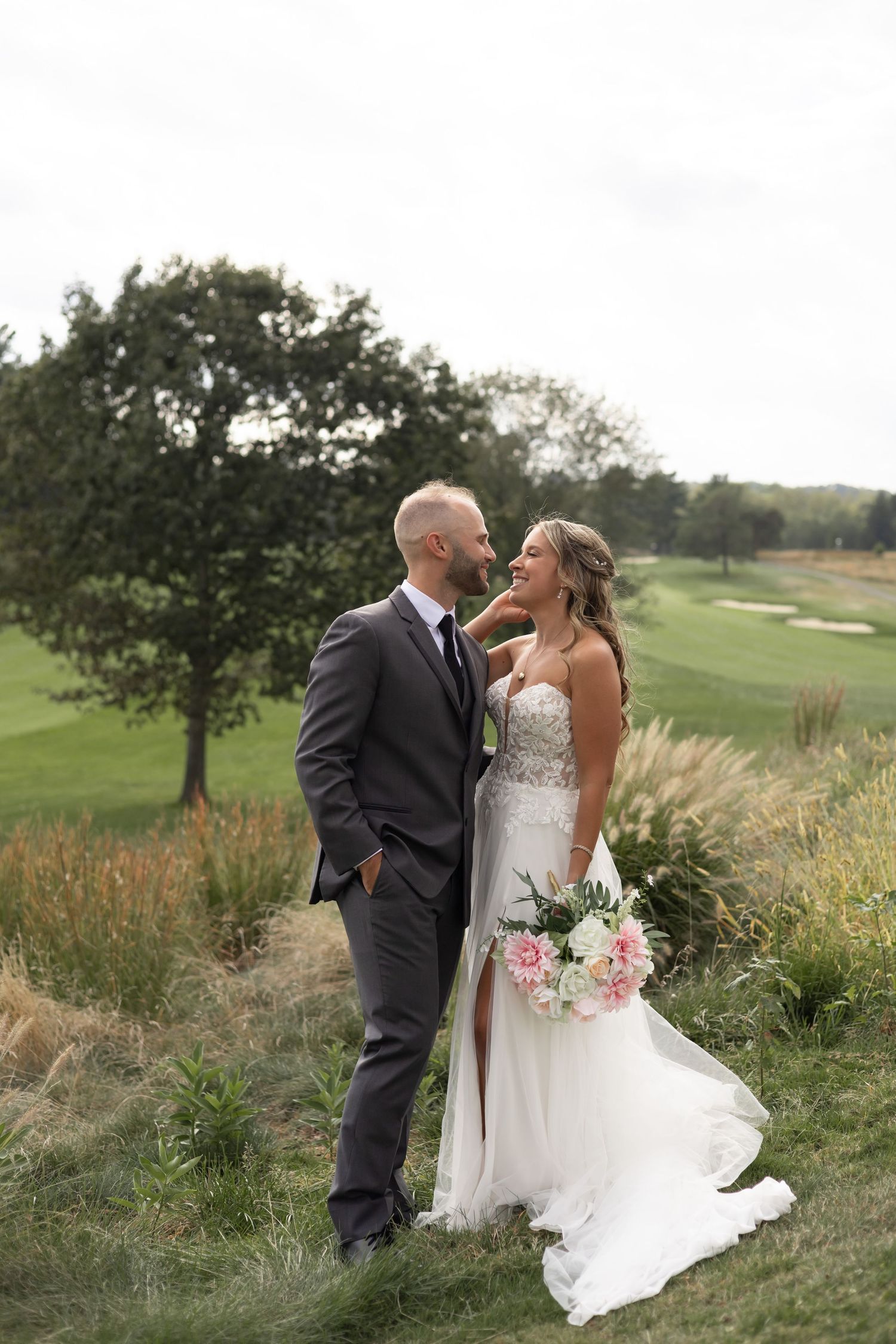 Wedding couple standing together on a golf course with ornate bouquet and flowing white gown against autumn landscape.