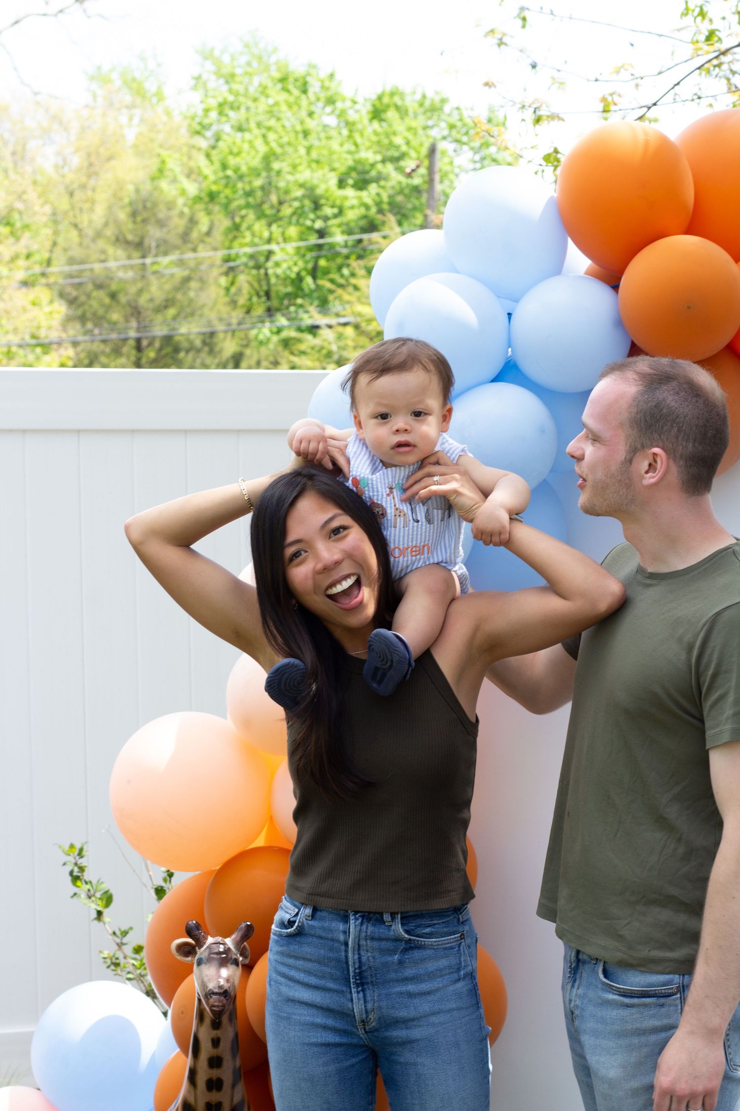 Family poses playfully together against white wall decorated with orange and blue balloons.