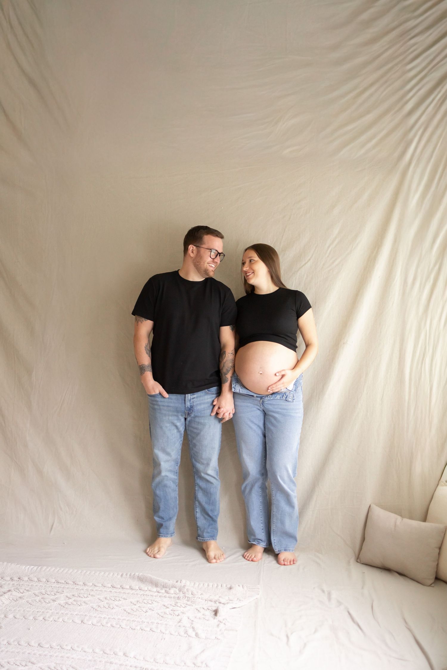 A series of minimalist maternity photos showing a couple in black shirts and jeans against a white backdrop.