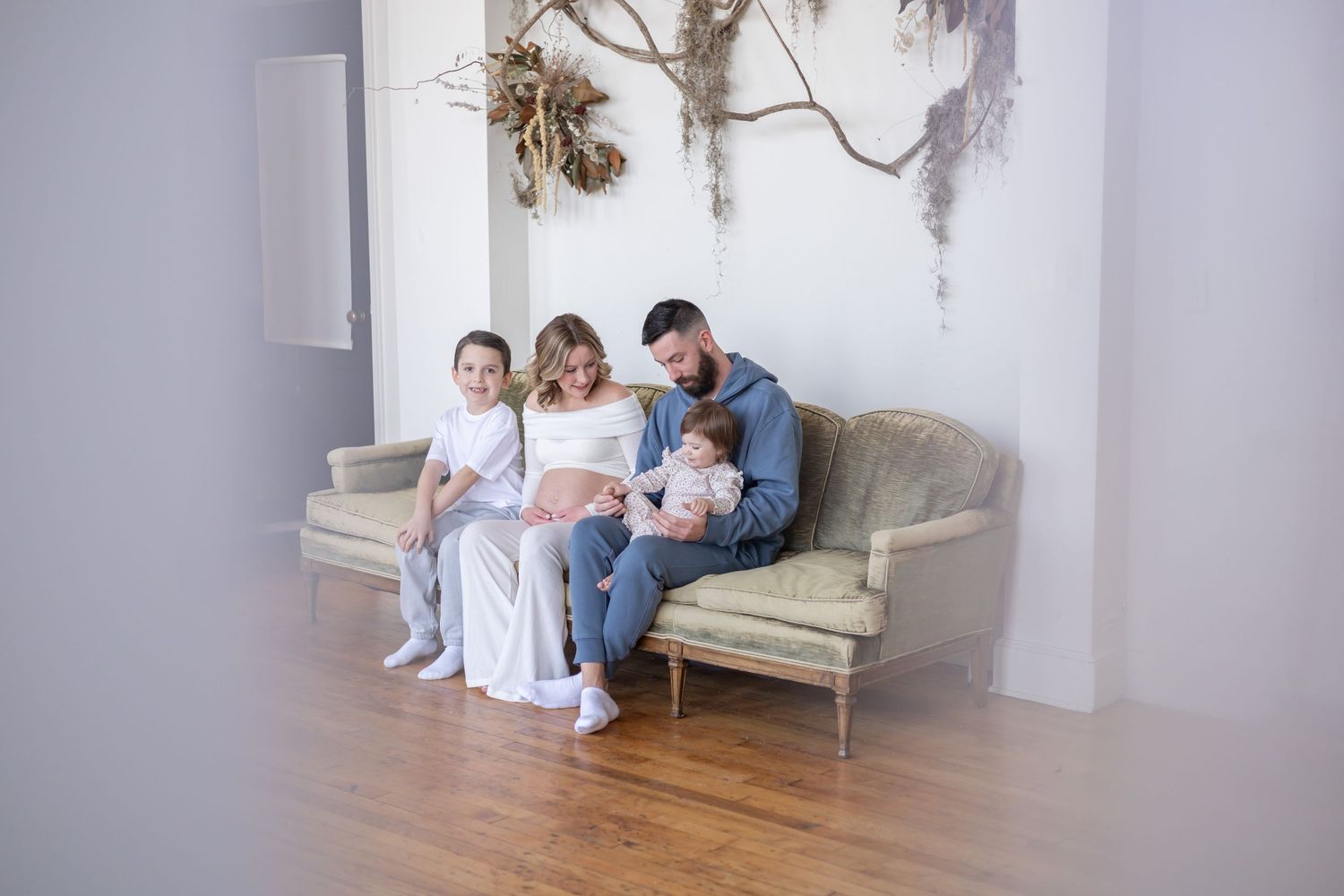 A family lounges together on a white couch in a bright, modern space decorated with neutral tones and minimal decor.