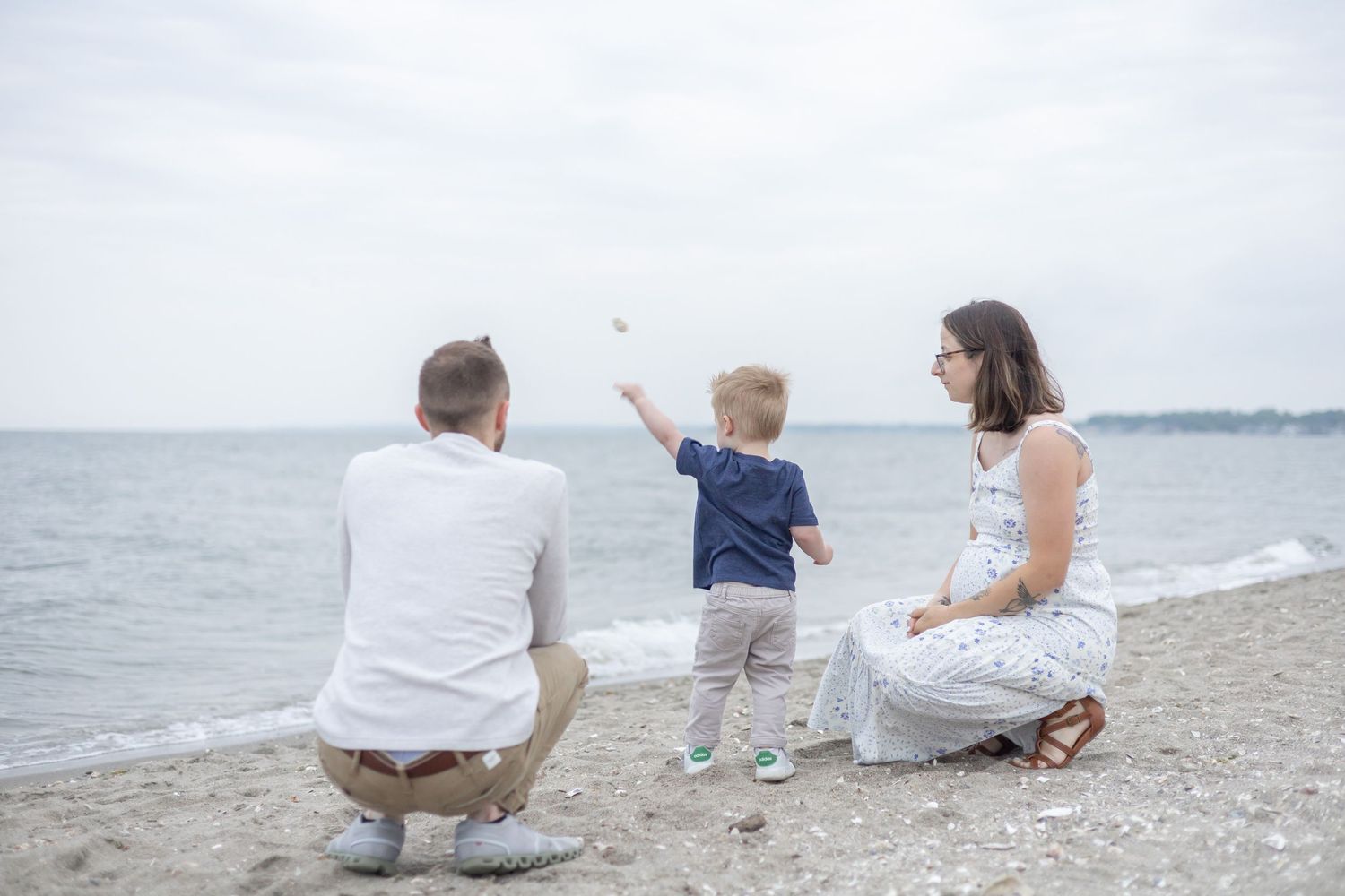 A family spending time together on a beach, pointing at something in the distance on a cloudy summer day.