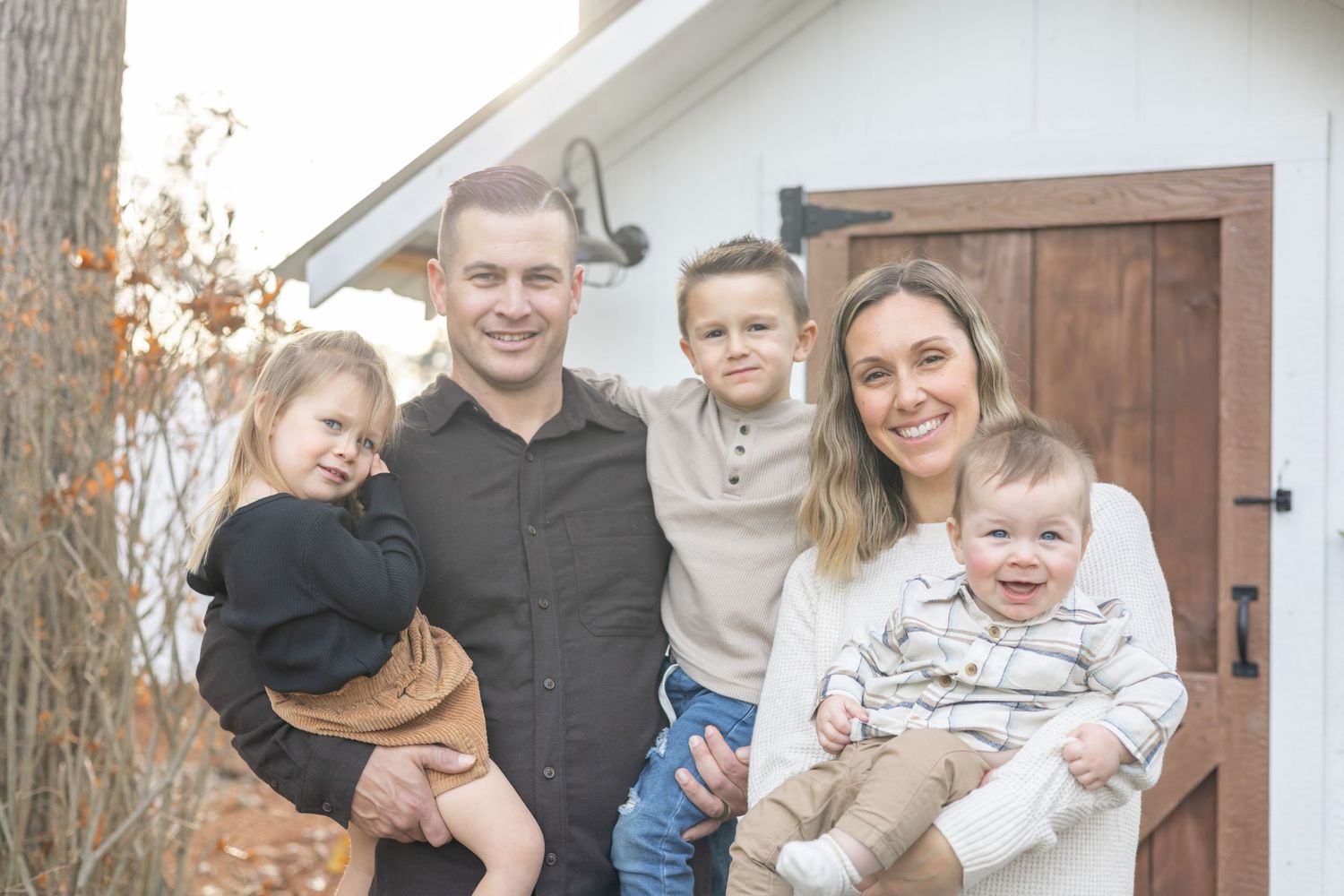 Casual family portrait in front of rustic wooden door on home exterior.