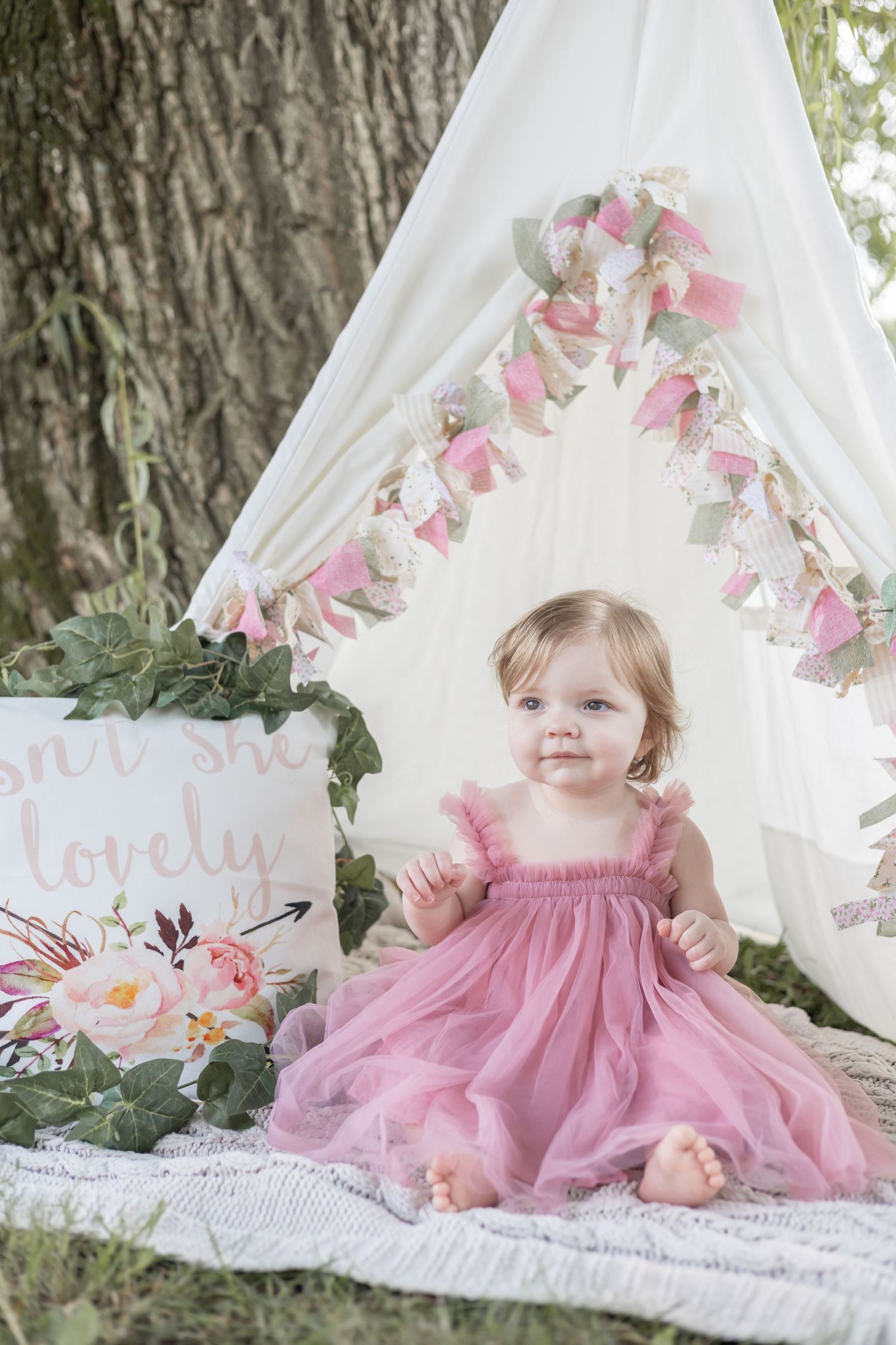 Beautiful pink teepee photo setup with floral garland and delicate decorations in an outdoor garden setting.