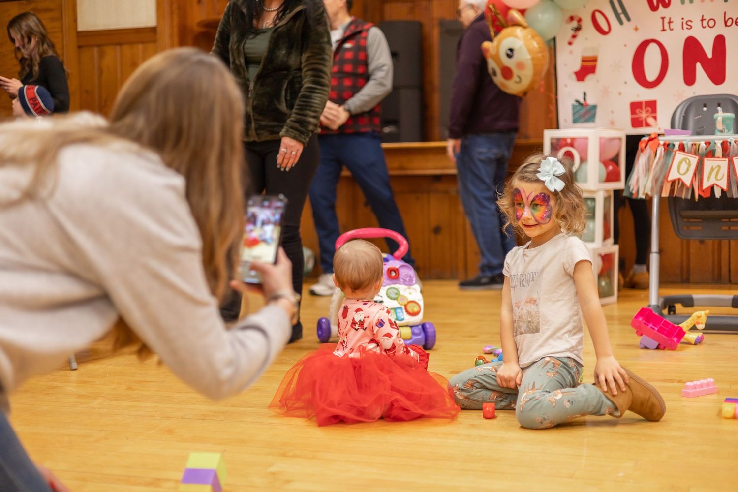 People gather in a community hall decorated with holiday decorations during a festive celebration.