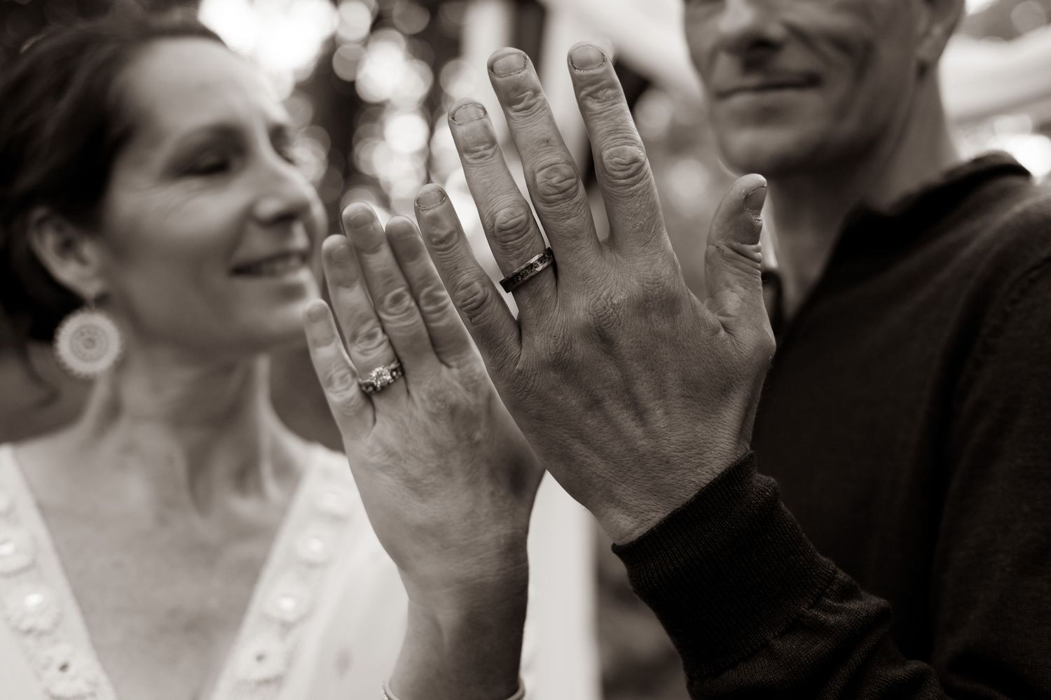 A black and white close-up of two hands showing wedding rings after an outdoor wedding ceremony.