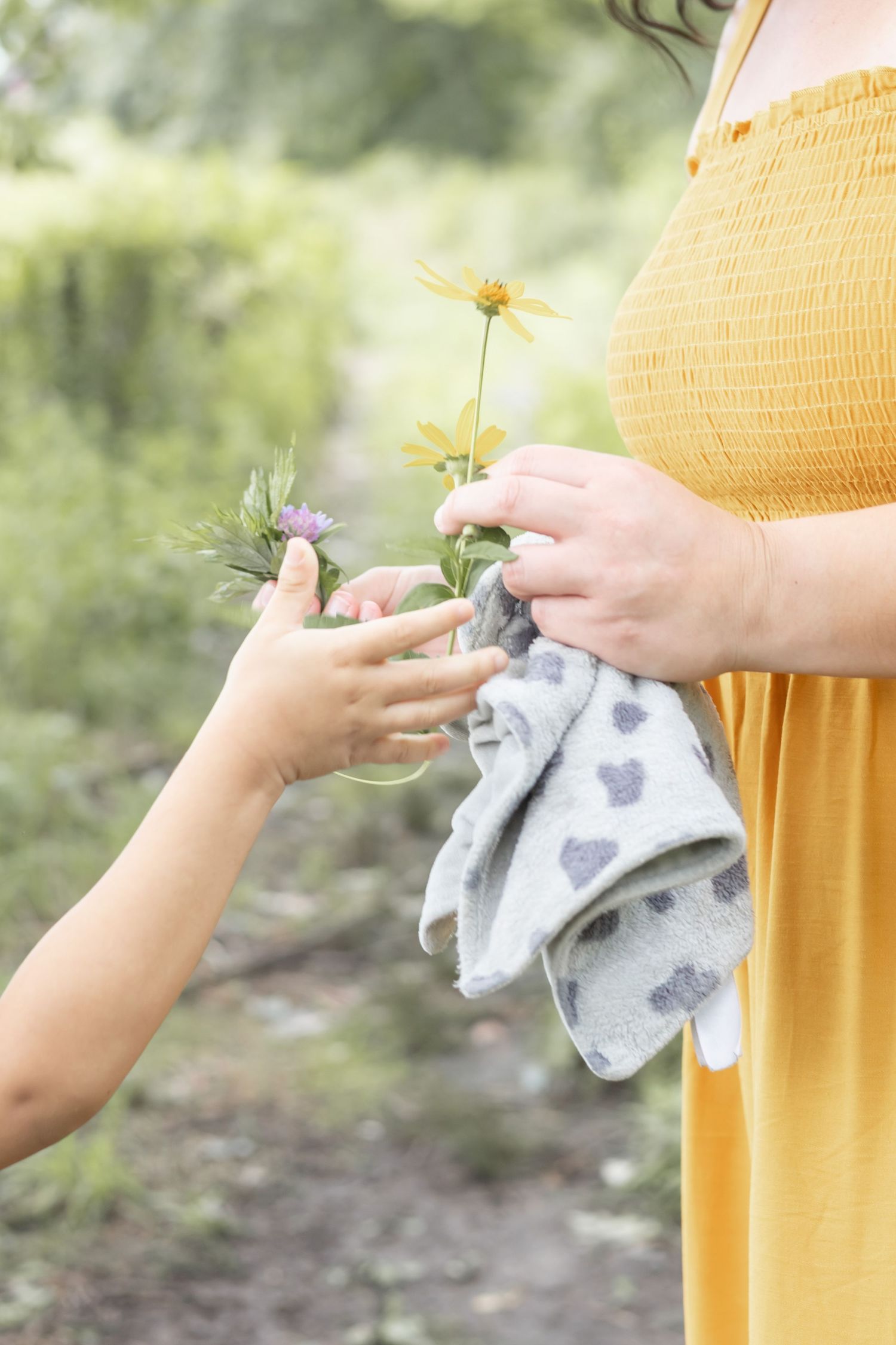 Close-up sequence showing hands in yellow dress folding a gray heart-patterned cloth in natural outdoor setting.