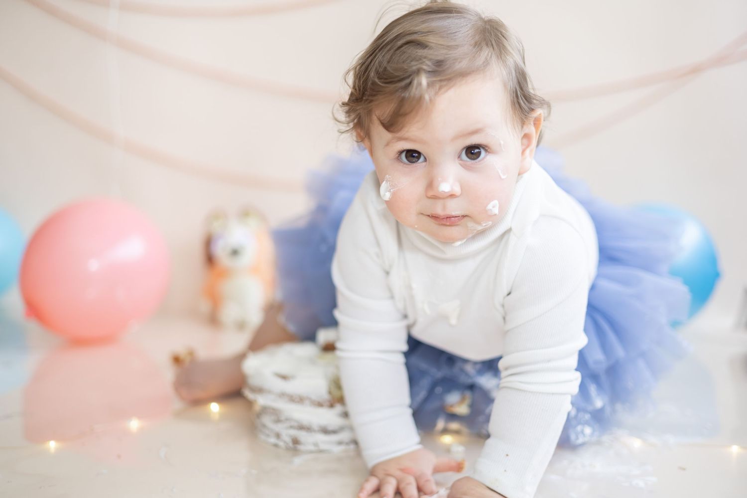A joyful child crawls on a soft carpet with colorful balloons in the background during a photo session.