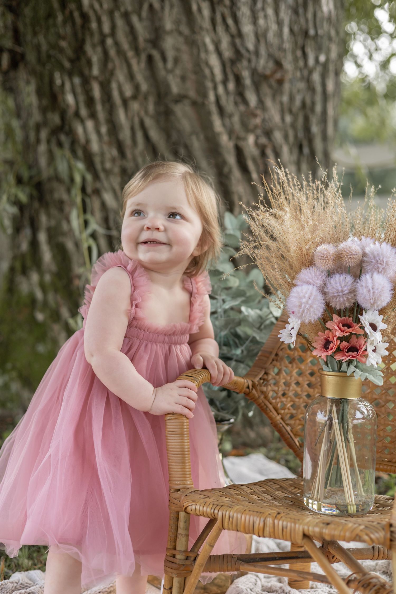 A child in pink tulle dress sits at outdoor tea party setting with wicker chairs and soft floral arrangements.
