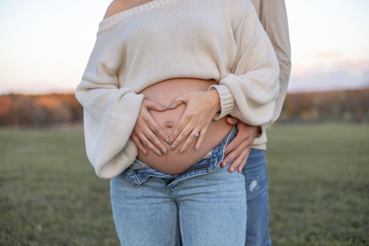 White sweater and blue jeans maternity outfit captured in natural outdoor setting.