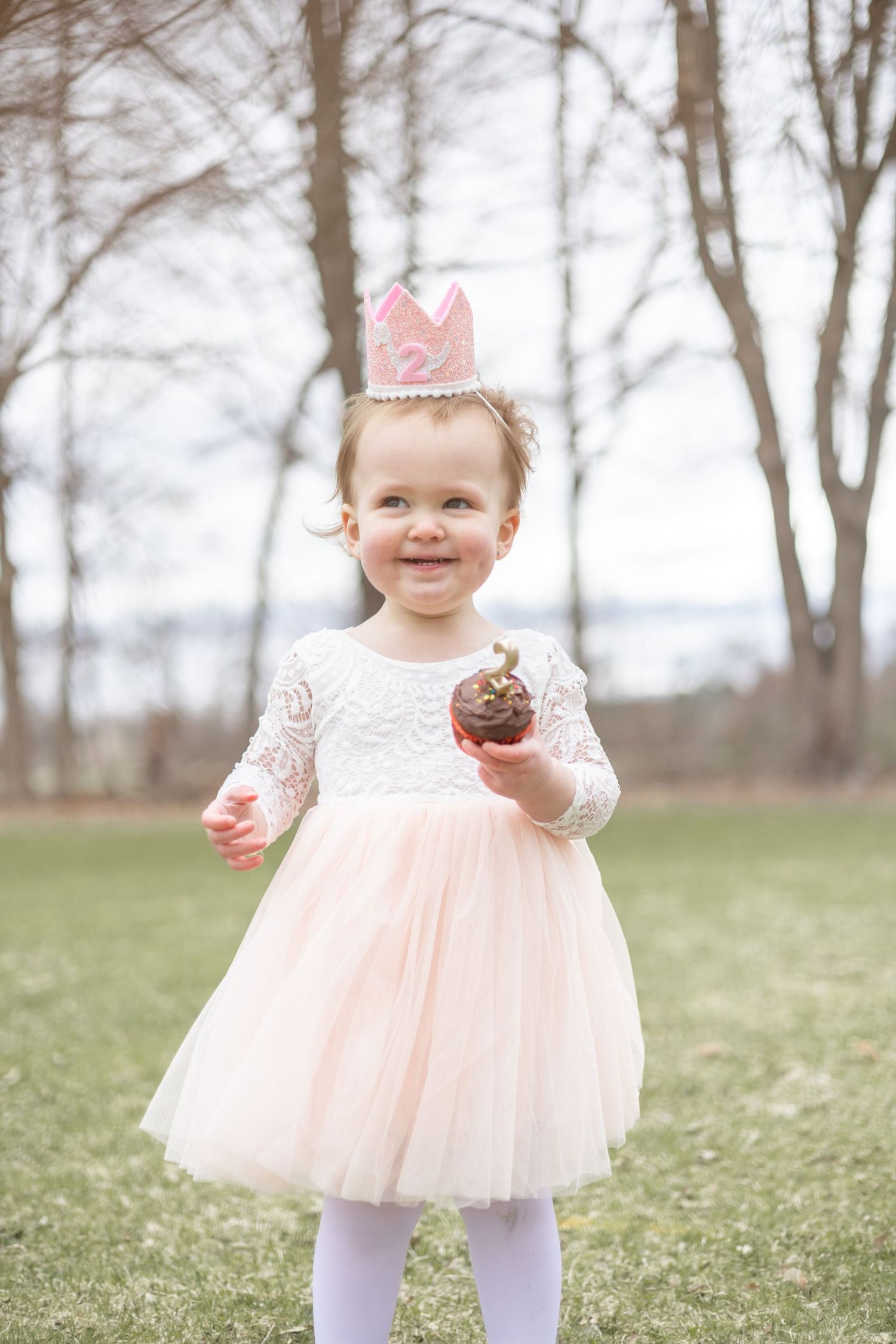 A child wearing a pink tulle dress and white tights twirls in a field on a foggy spring day.