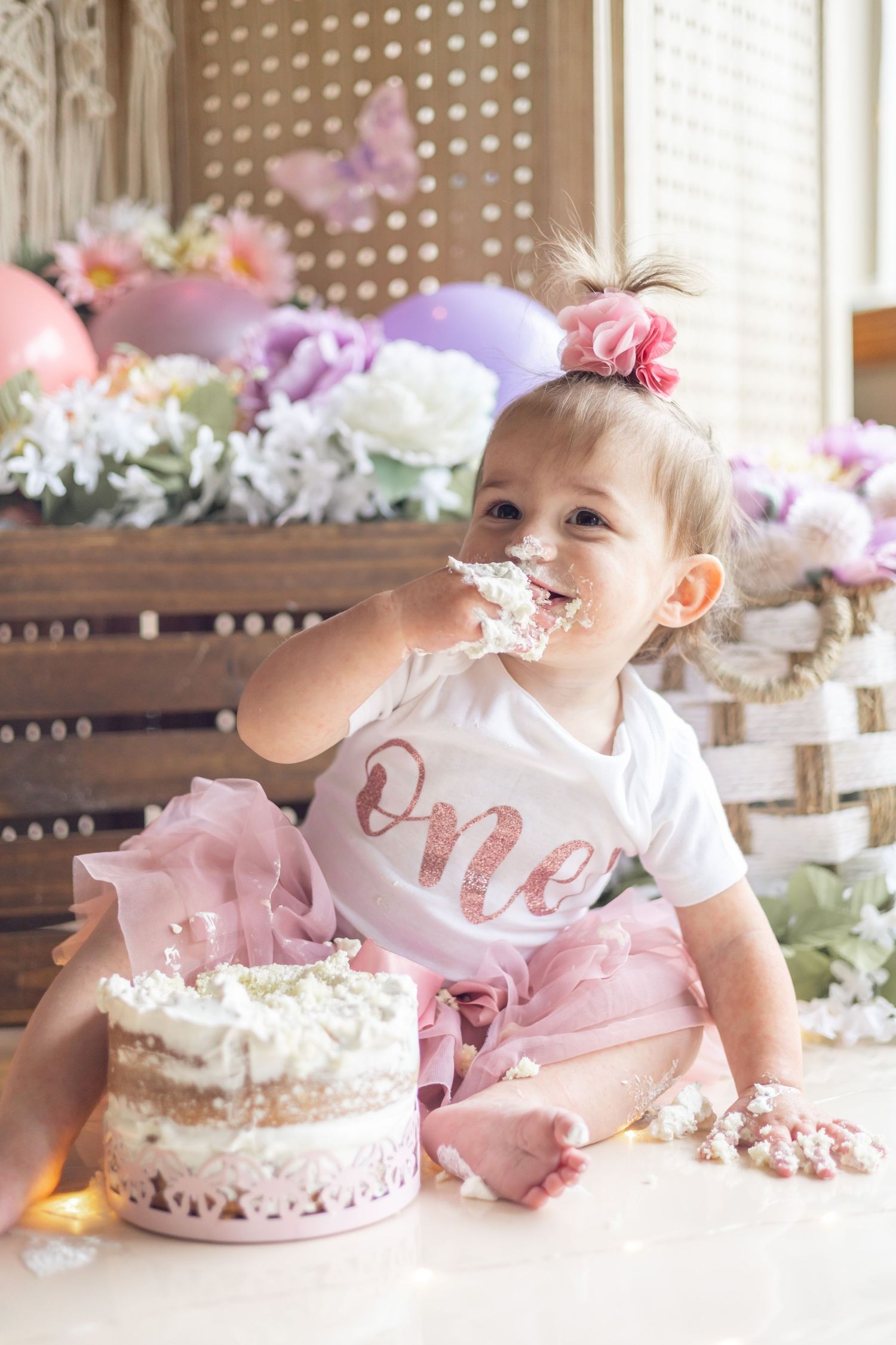 A series of first birthday cake smash photos featuring pink and white decorations with floral accents and a frosted cake.