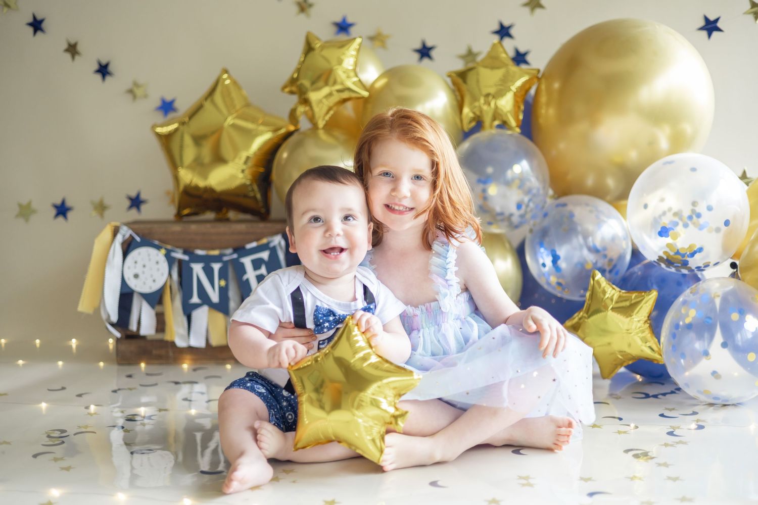 Golden star balloons and blue banner decorations create a festive party setting against a white background.