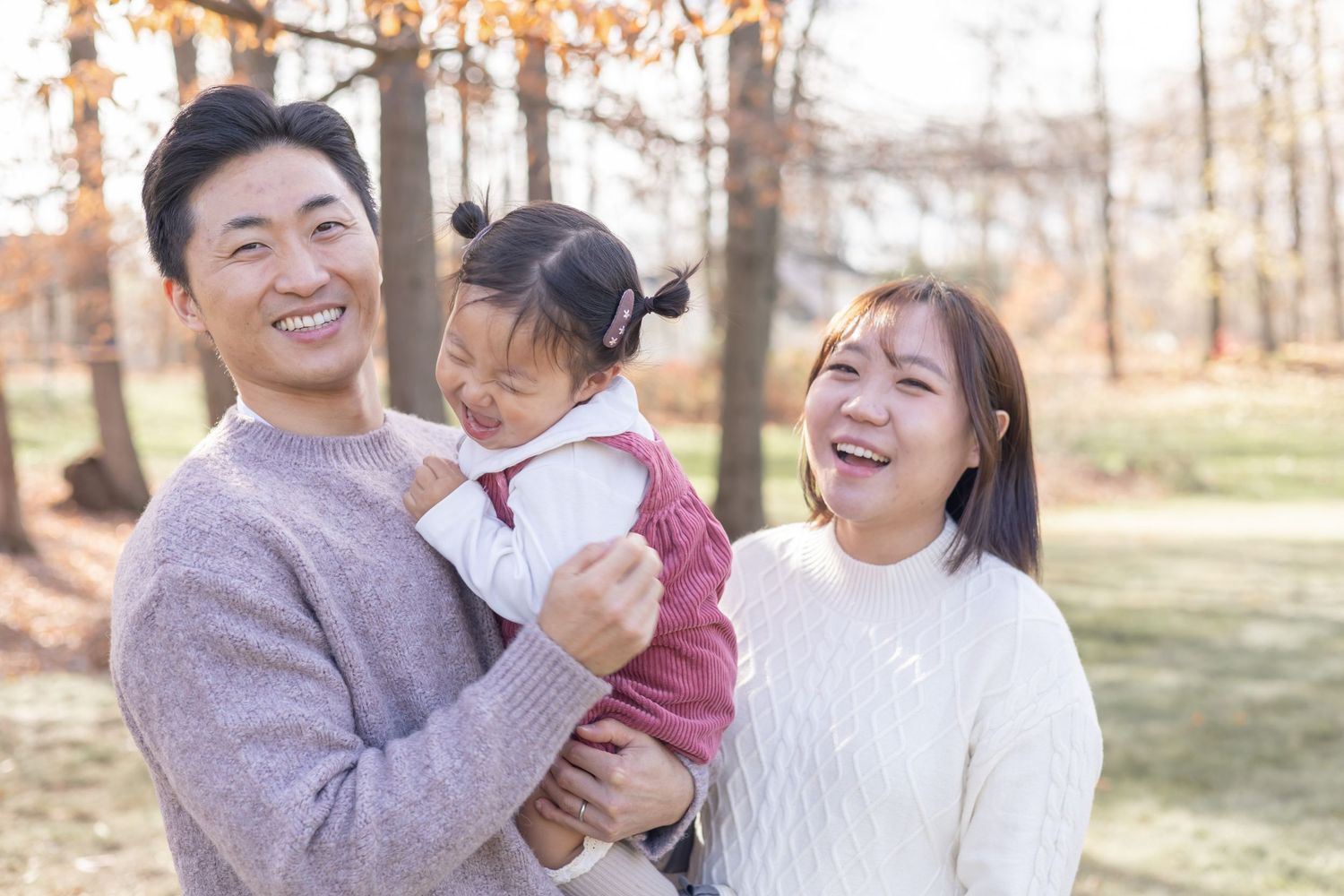 A family in white and grey sweaters enjoys quality time together outdoors on a sunny autumn day in the park.