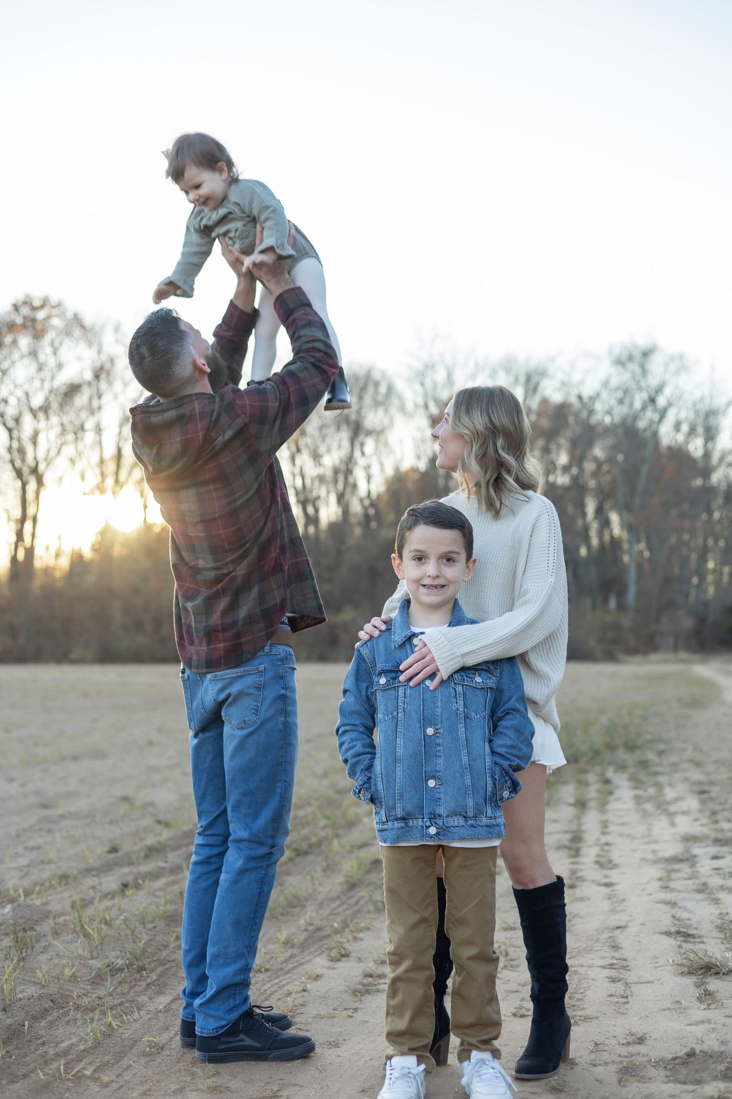 Family enjoying a golden sunset moment in a field with casual denim and plaid outfits.