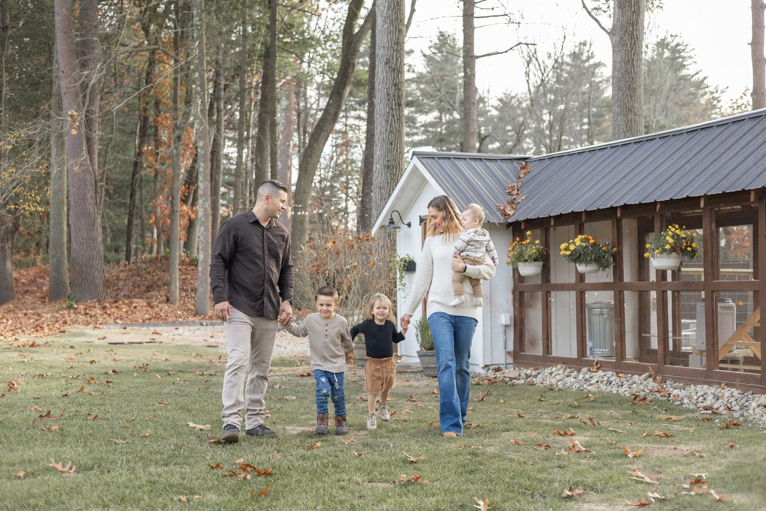 People walking and gathering outdoors among pine trees in a wooded area.
