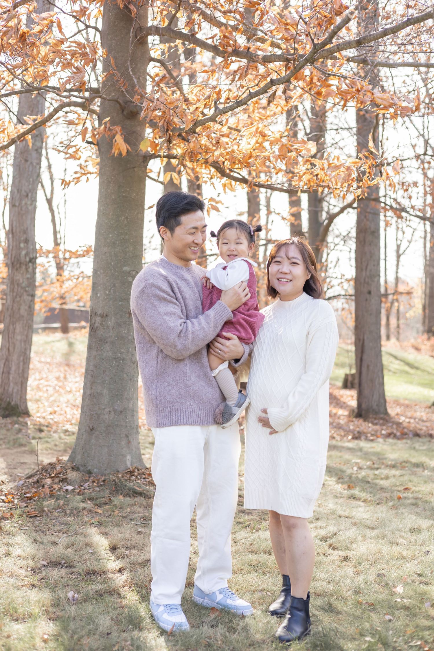 A group in white clothing embraces in a wooded autumn setting with golden leaves and soft sunlight.
