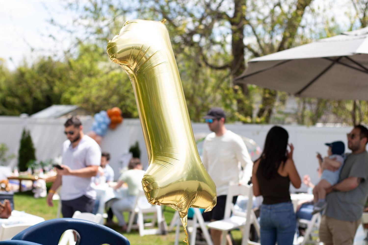People enjoying outdoor party with a gold balloon decoration and white tents in a park setting.