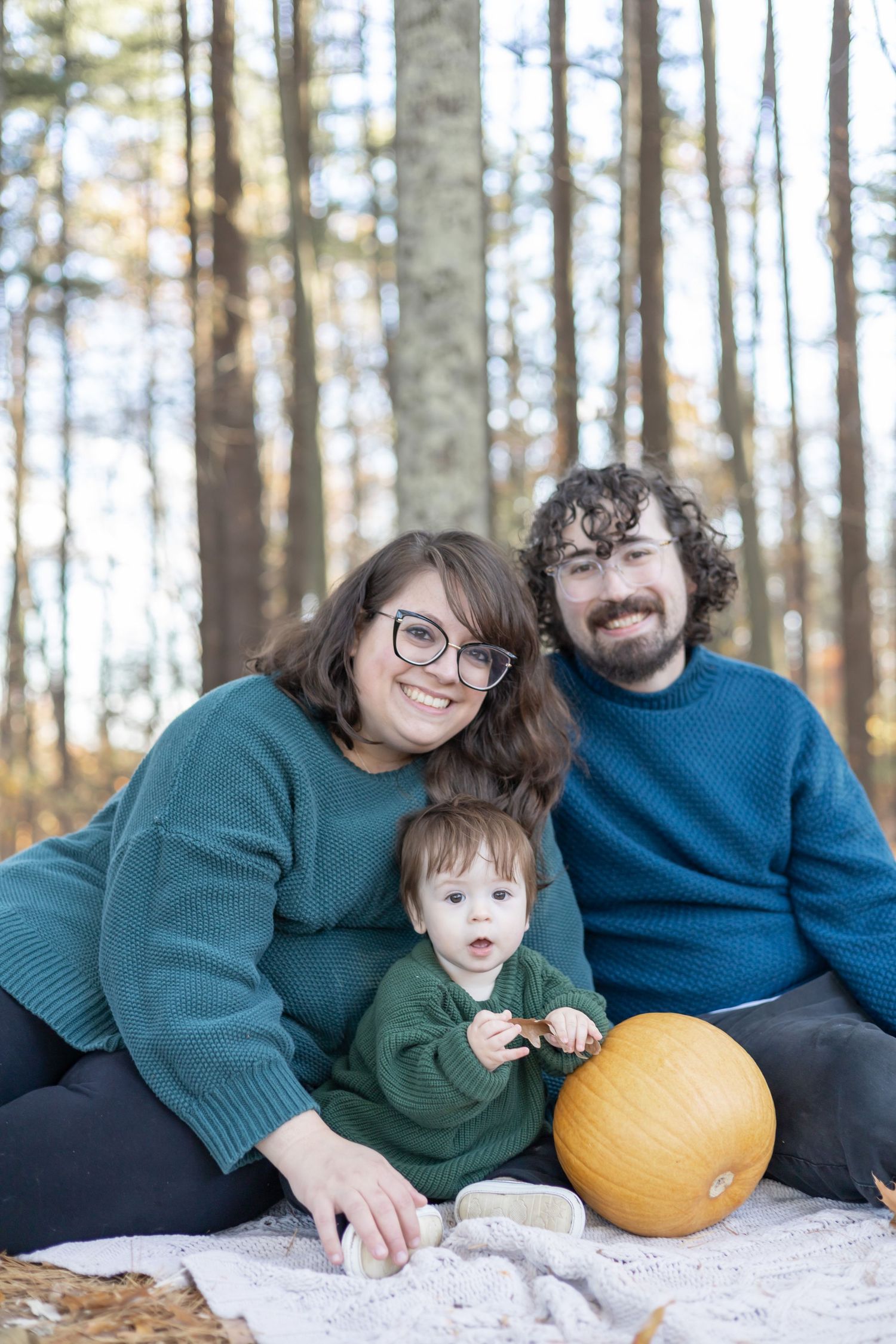 Family in winter forest scene sharing heartwarming moments as they inspect a bright yellow pumpkin together.