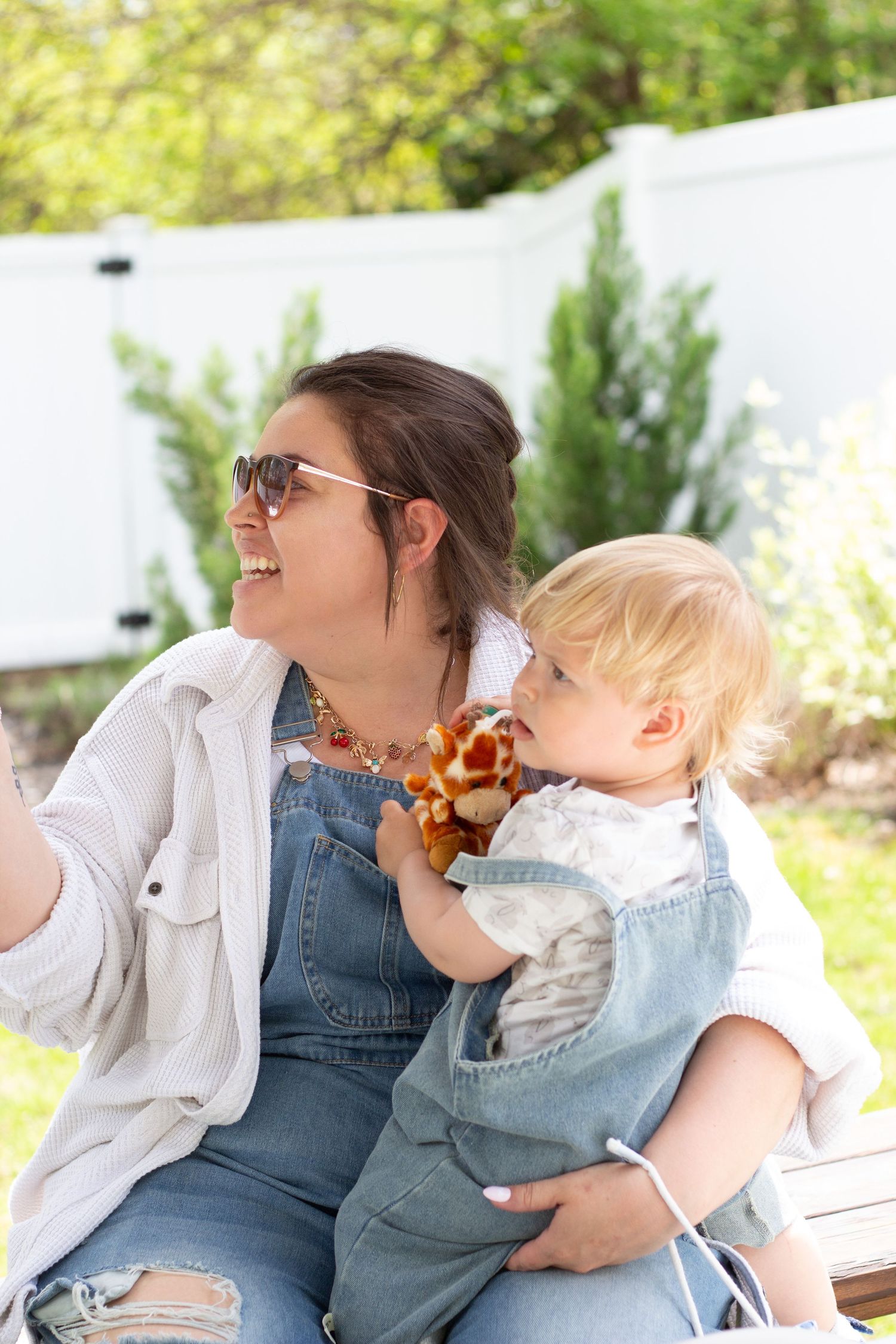 Two people in matching denim overalls sit together outdoors on a sunny day while enjoying a fun moment.