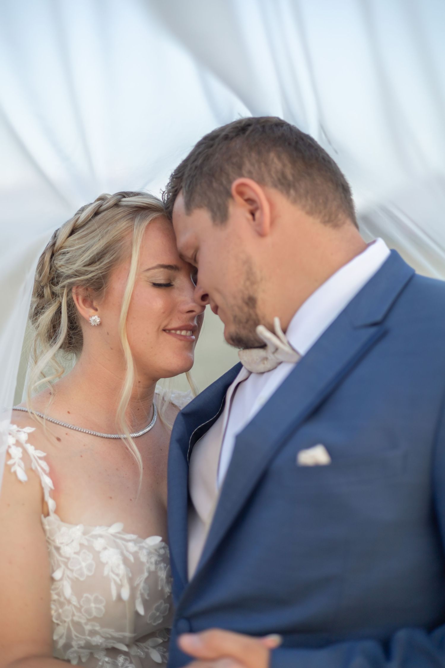 A tender moment between newlyweds sharing a close embrace, with the bride in lace and groom in navy blue suit.
