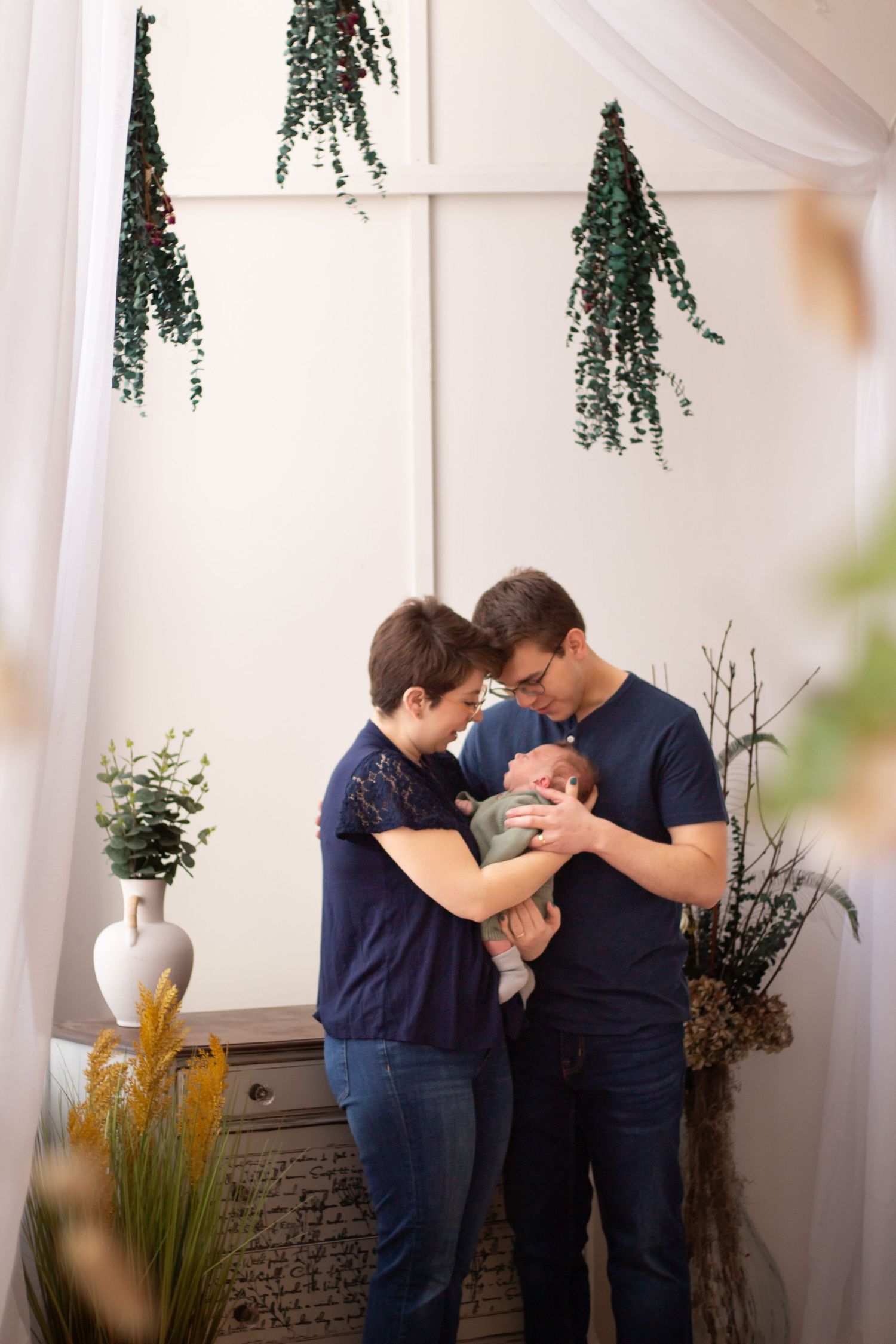 Couple shares an intimate moment in an elegantly decorated white room with hanging greenery and stone accents.