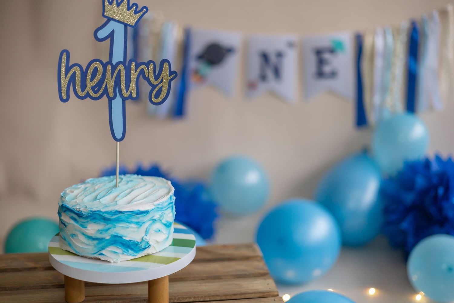 A festive birthday party setup with blue balloons and cake decorations featuring crowns and gold accents.