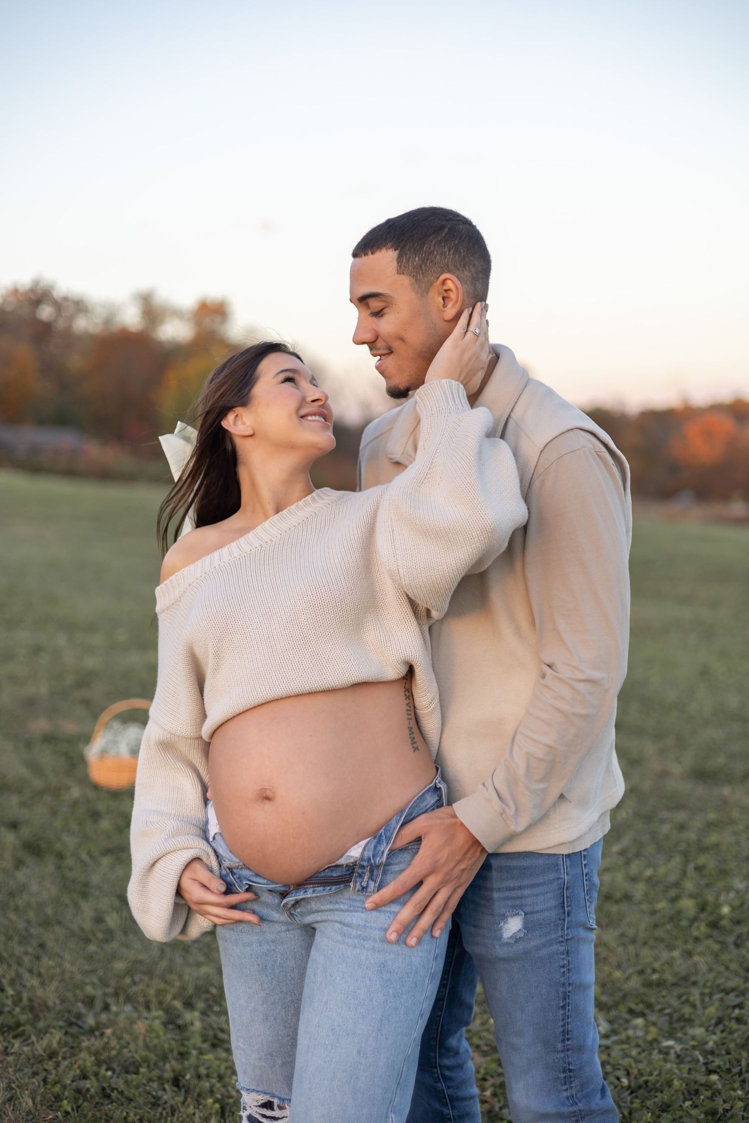 Casual maternity photo of expecting couple laughing together in autumn field setting.