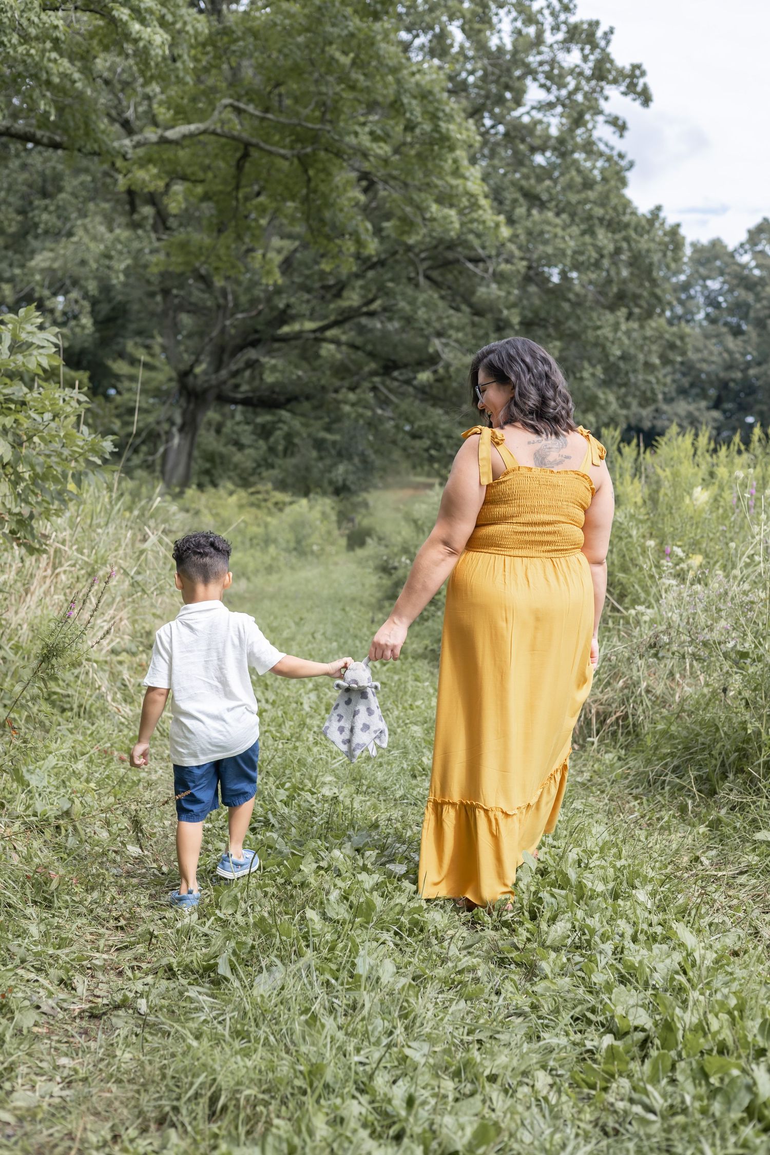 Woman in yellow dress and child walking together through a lush green field holding hands on a summer day.
