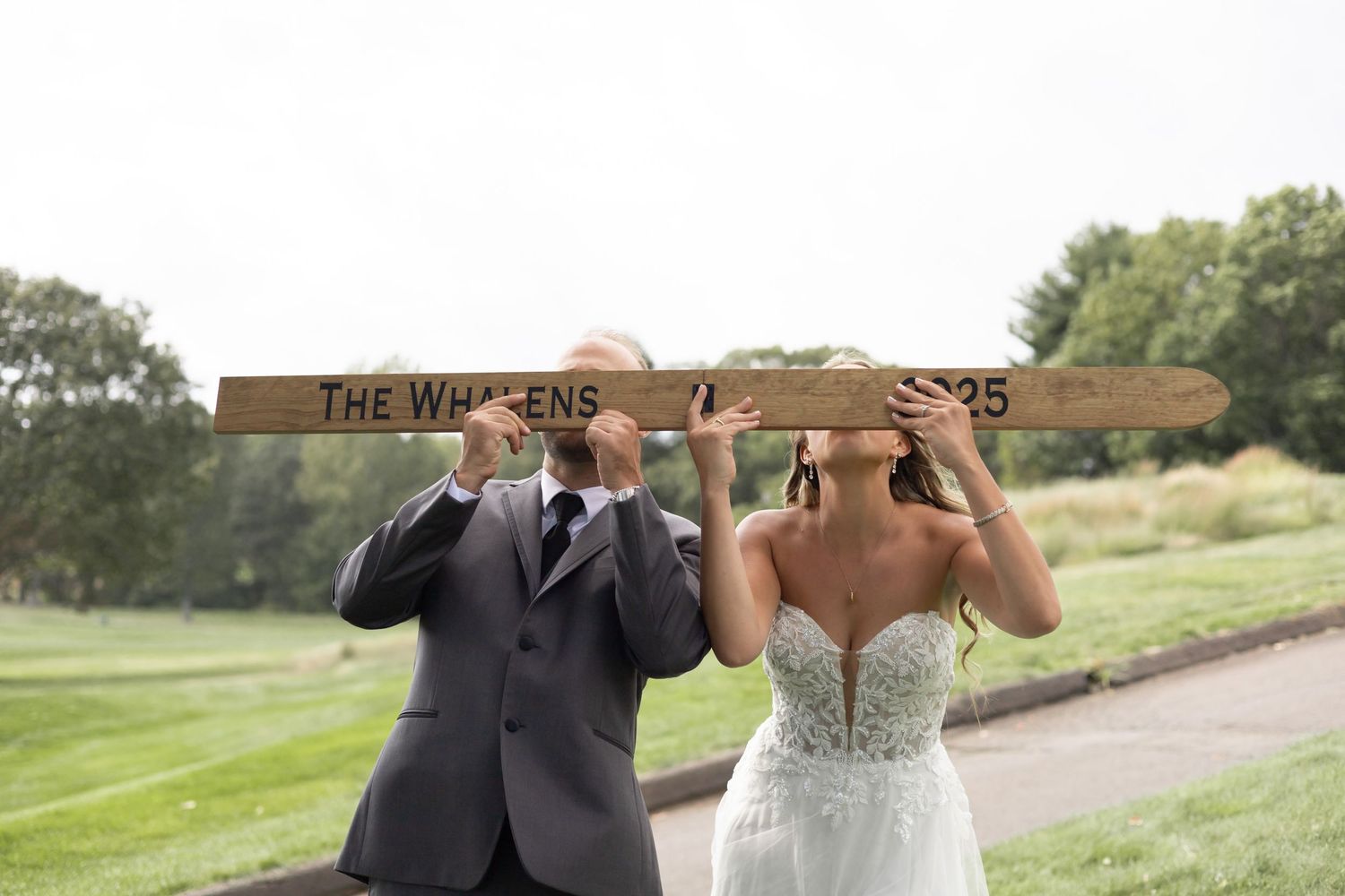 A couple poses together on a sunny golf course with elegant wedding attire and lush greenery in the background.