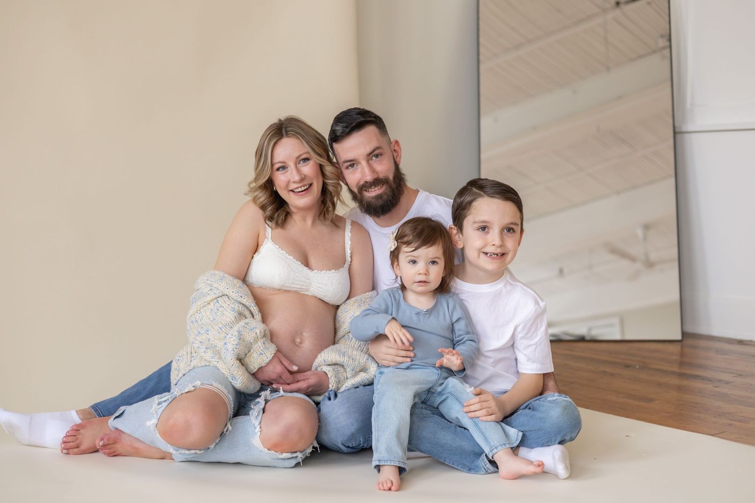 A family wearing casual white and denim outfits sits together on the floor of a bright interior space.