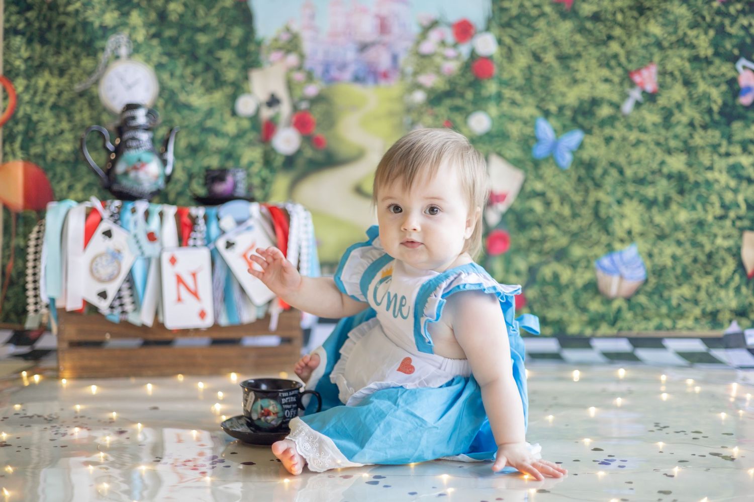 Small child in blue dress sits on floor with butterflies and party decorations during festive celebration.