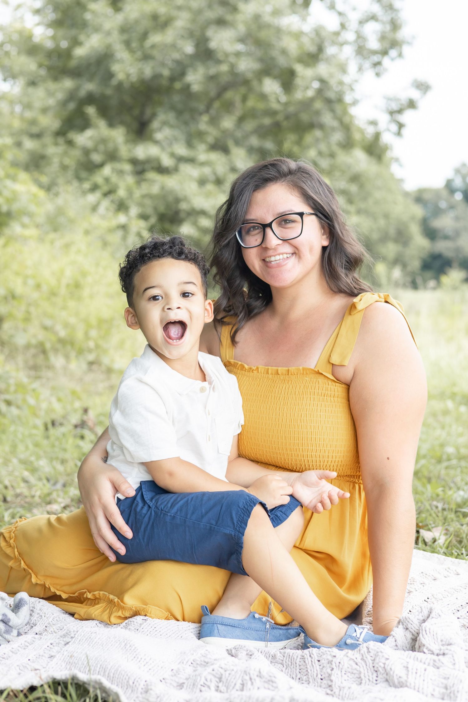A parent and child sit together outdoors in casual attire on natural terrain, smiling and interacting in a series of photos.