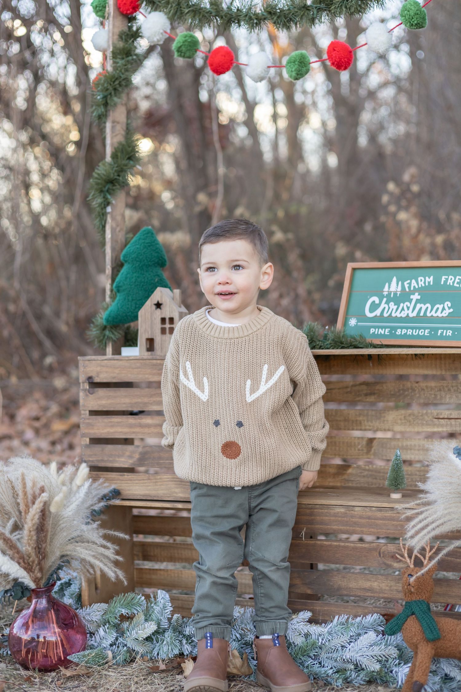 Festive holiday scene with wooden crates, decorated with ornaments and garland, featuring a reindeer sweater and chalkboard sign.