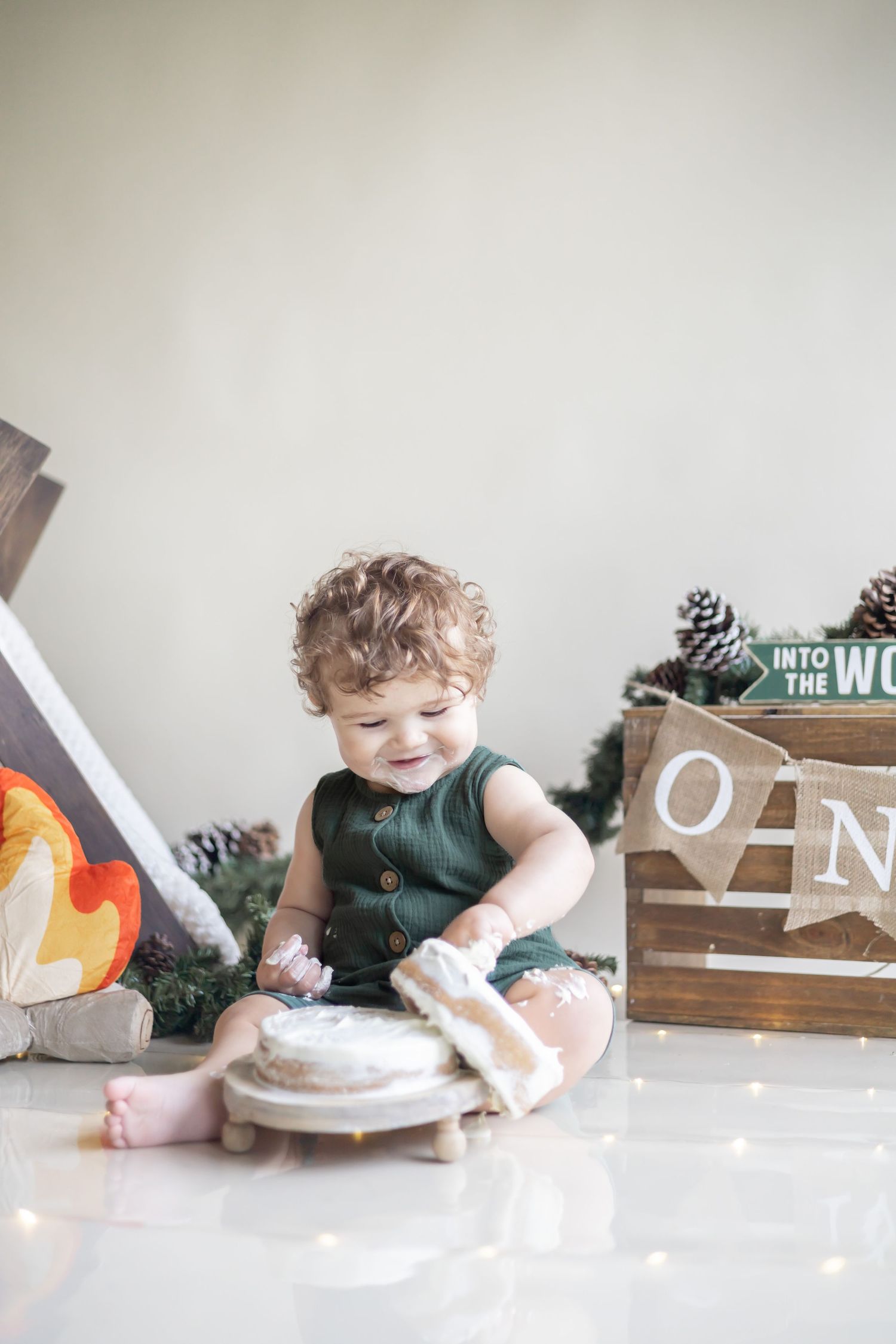 Small child wearing green sits on floor playing with rustic decorative items near wooden box with pinecones.