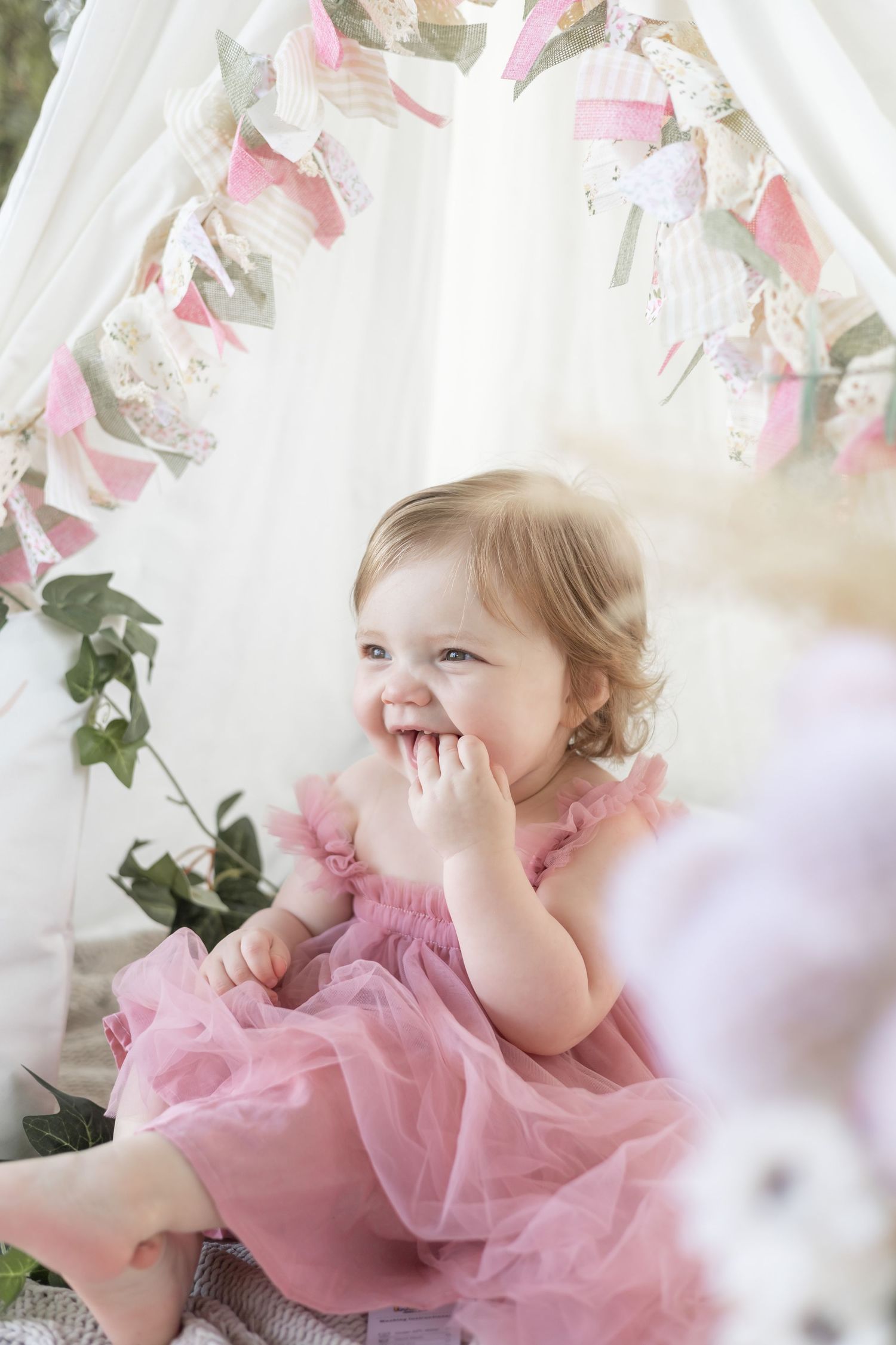 A young child in a pink tulle dress plays and giggles while surrounded by delicate floral decorations.