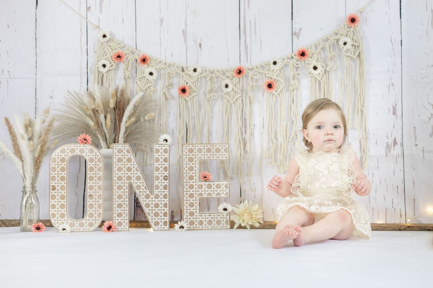 Rustic inspired cake smash photo session setup with white wood backdrop, peach flowers, and wheat grass decorations.