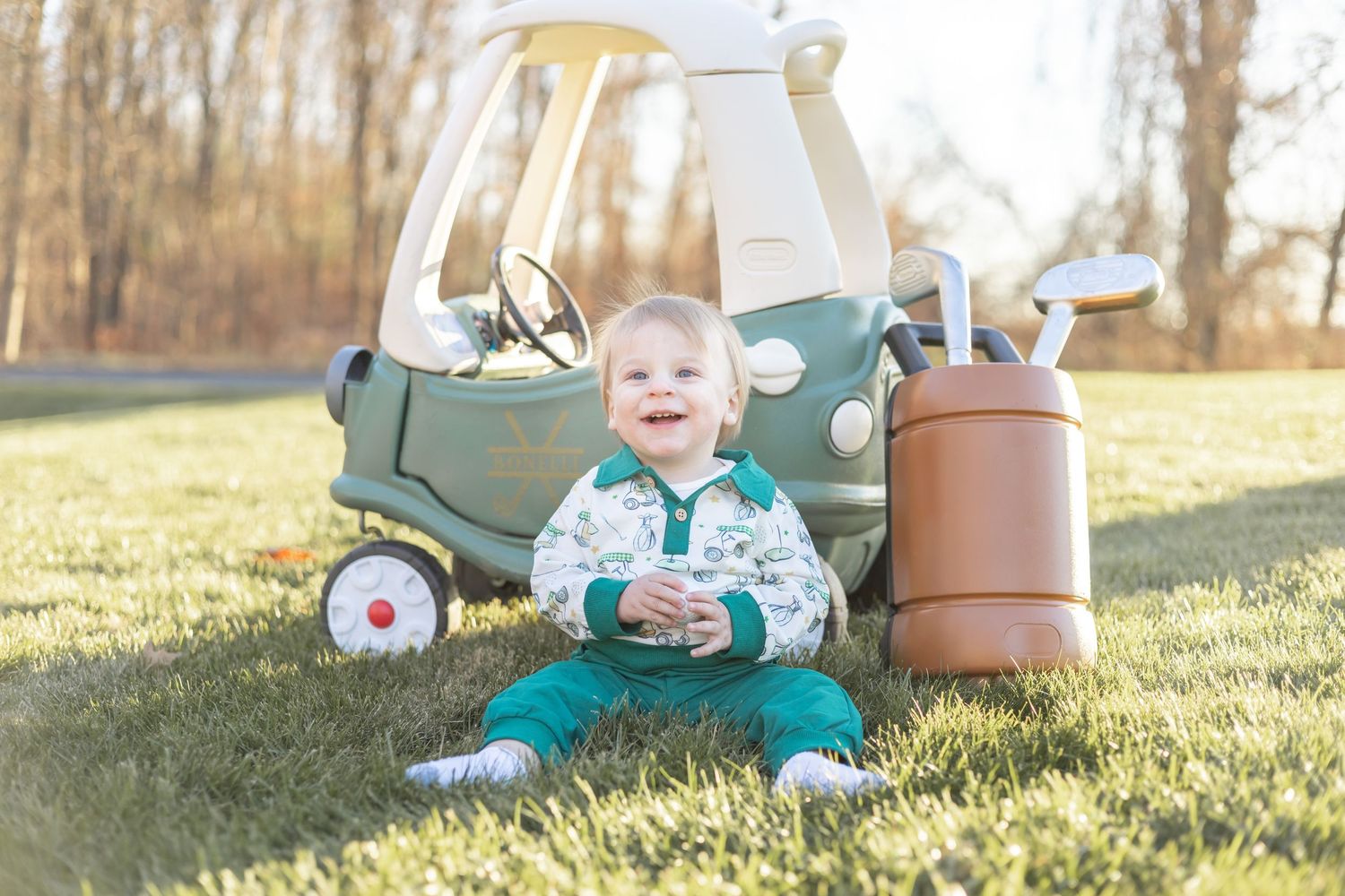 Young child plays outdoors on grass while sitting next to brown planter pots on sunny autumn day.