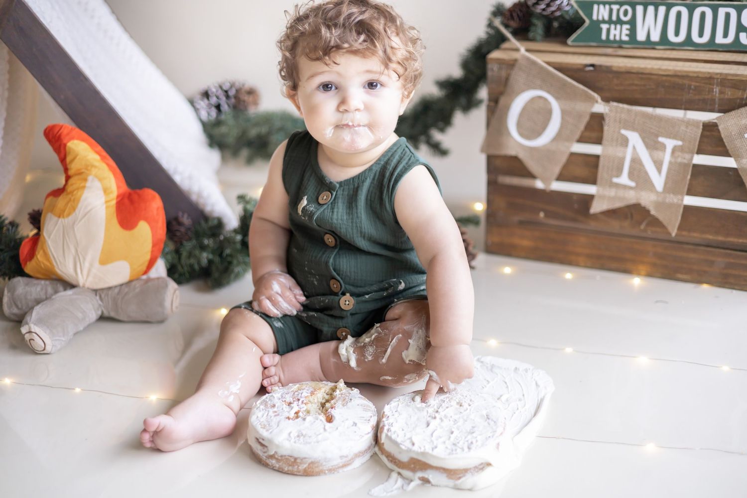 Small child sitting on floor beside wooden decor and orange flame decoration for first birthday celebration.