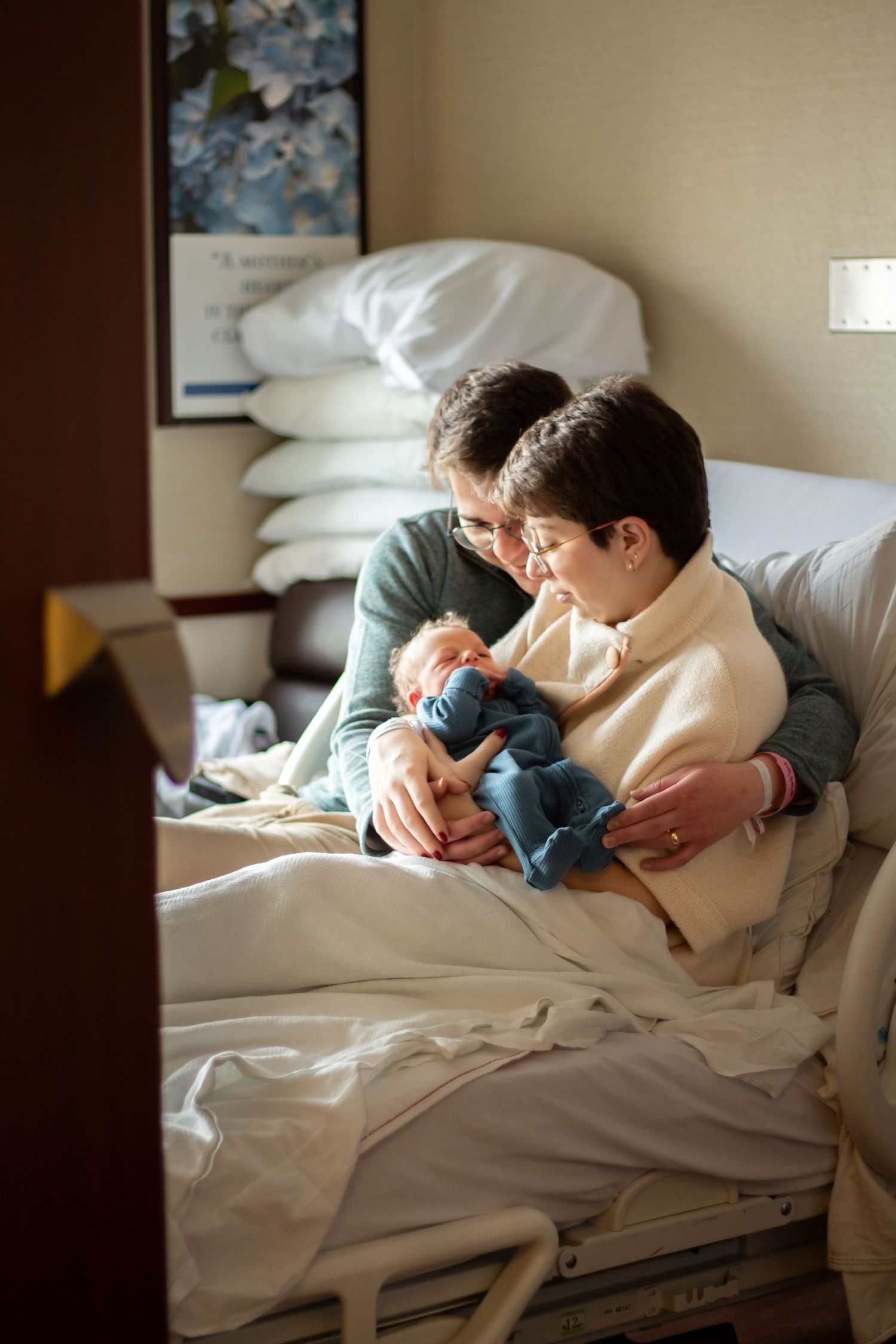 Tender moment in a hospital room as adults hold and comfort a small baby together on a medical bed.