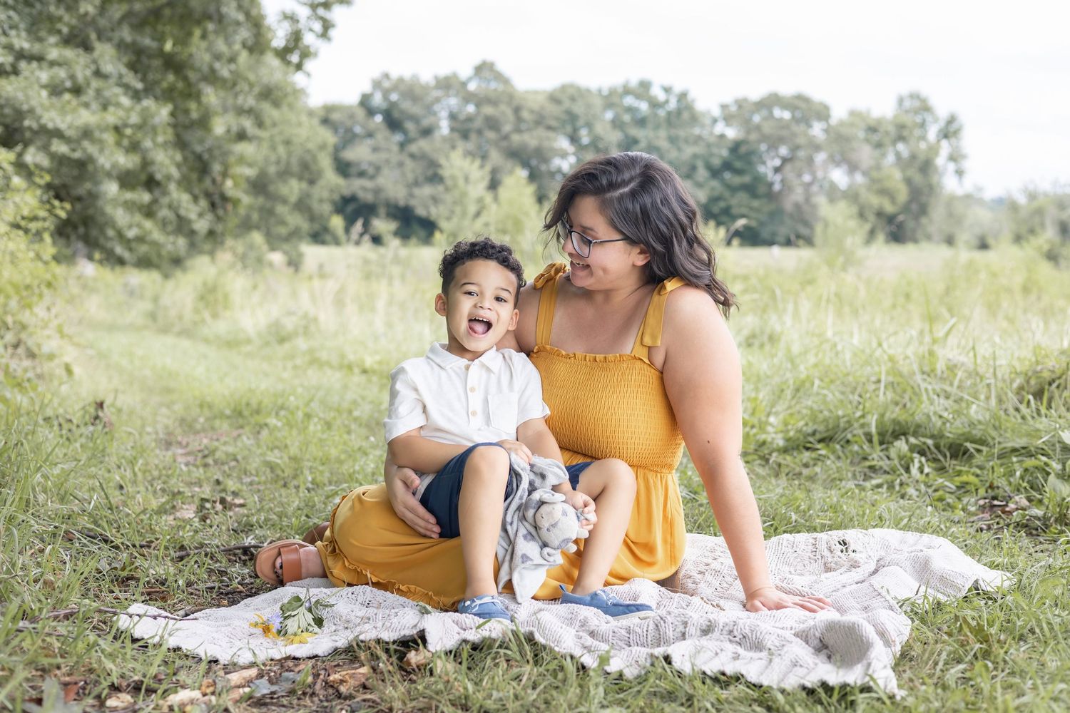 A joyful outdoor picnic scene on a white blanket in a sunny meadow with trees in the background.