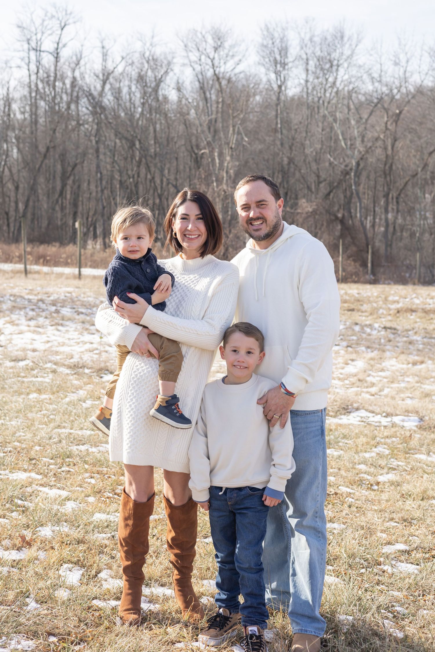 A family stands together outdoors on a winter field with bare trees in the background.