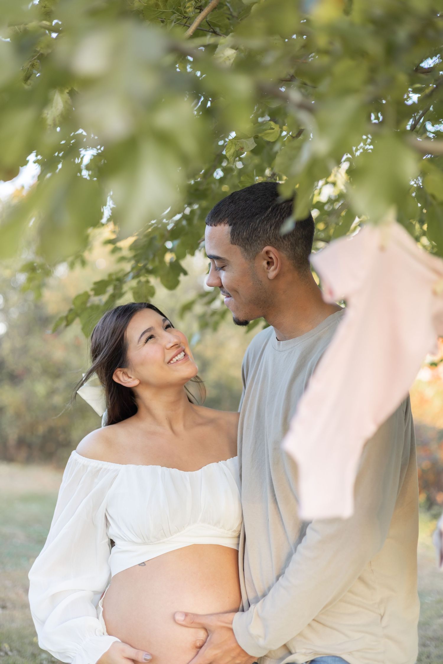 Romantic outdoor maternity photo with couple embracing under tree branches and soft lighting.