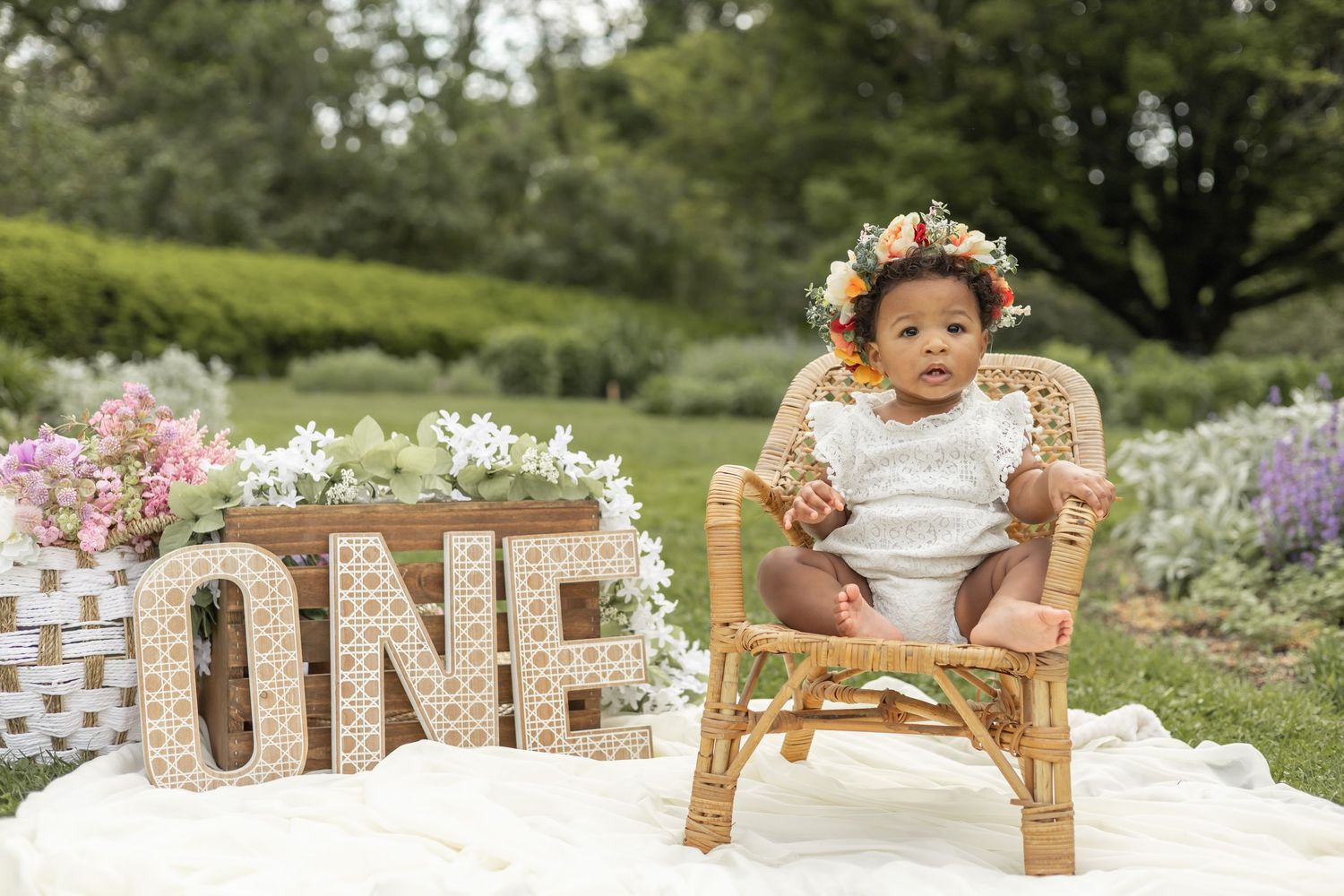 Outdoor newborn milestone photo session setup with rustic wooden furniture and soft pink floral decorations in a garden setting.