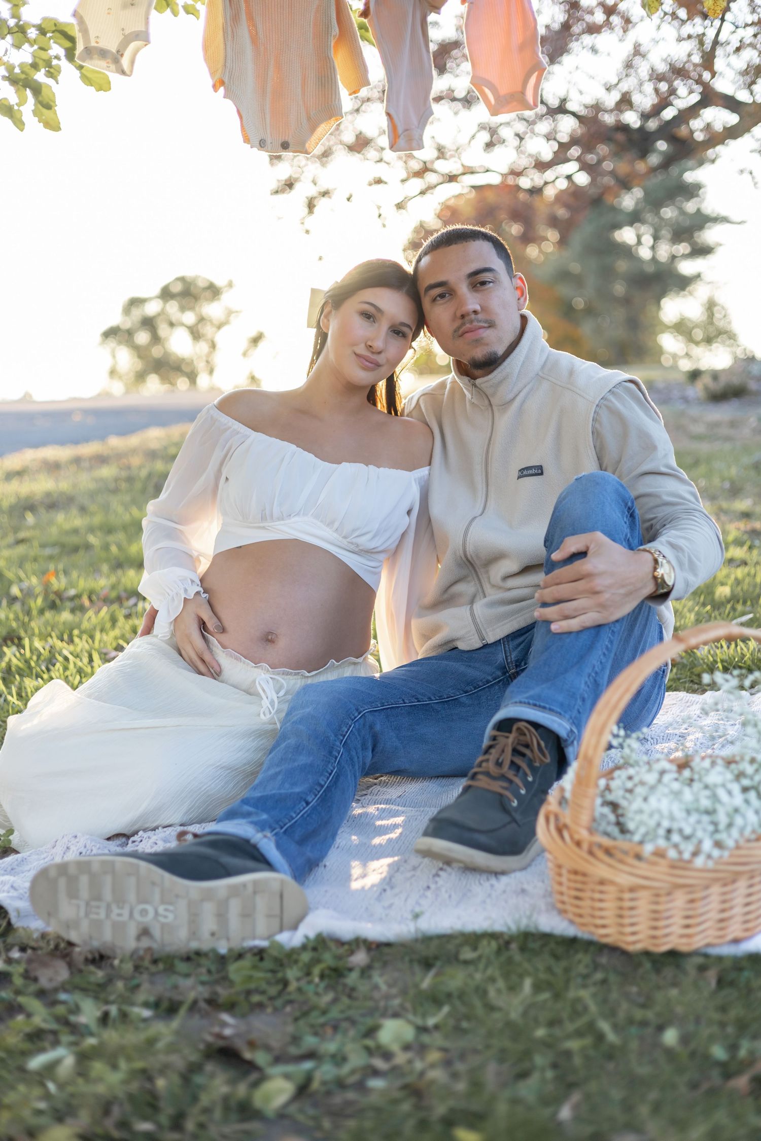 Intimate maternity photoshoot of couple relaxing on a picnic blanket during golden hour with wicker basket.