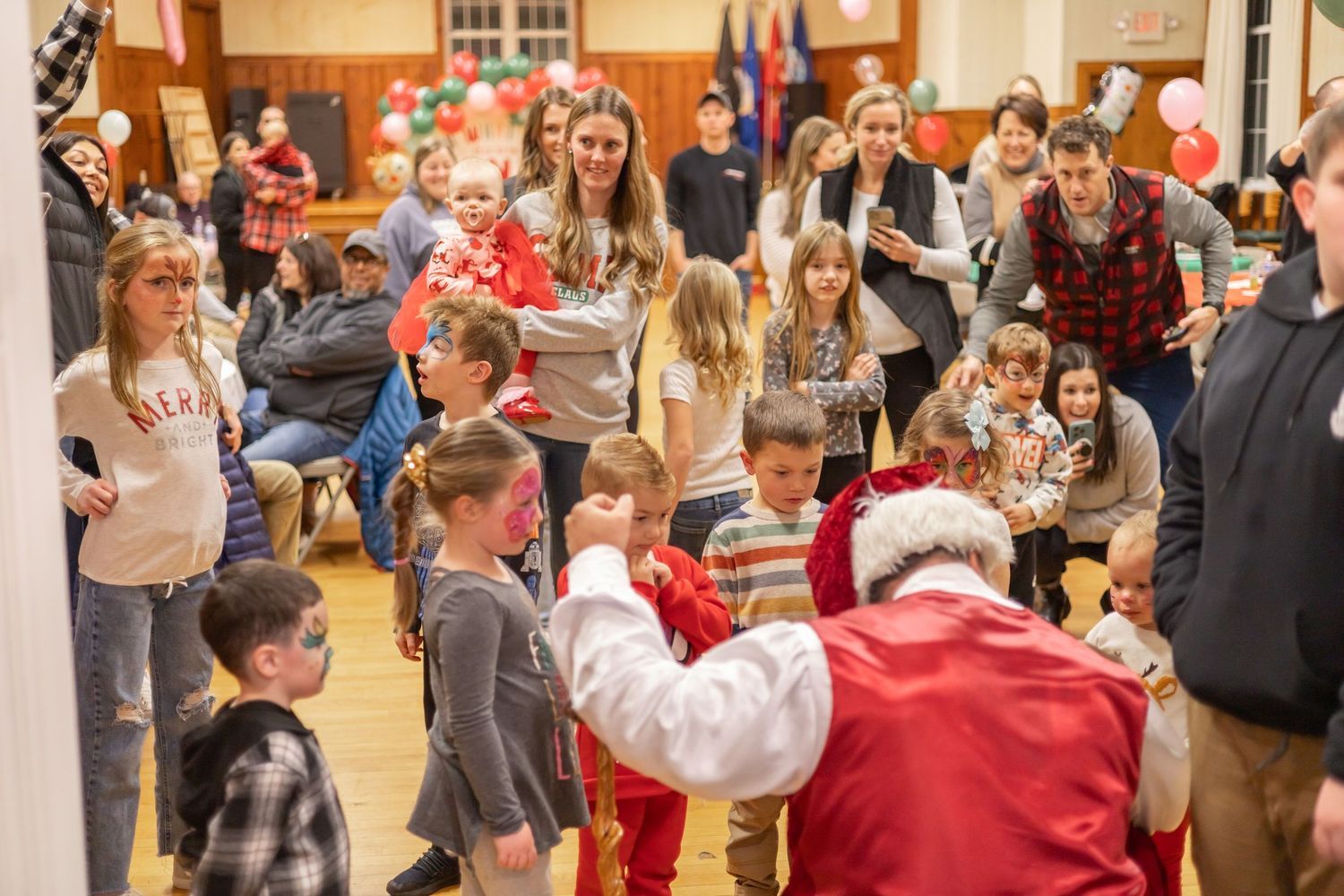 Large group of families gathered in a community center hall during a festive holiday celebration.