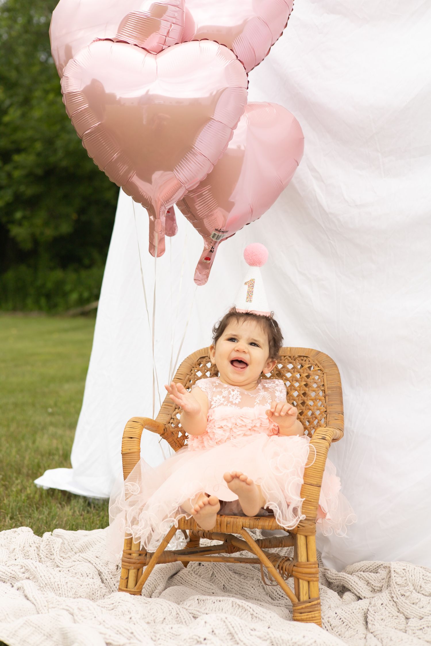 Small rocking chair decorated with pink heart balloons and white fabric for a festive celebration outdoors.
